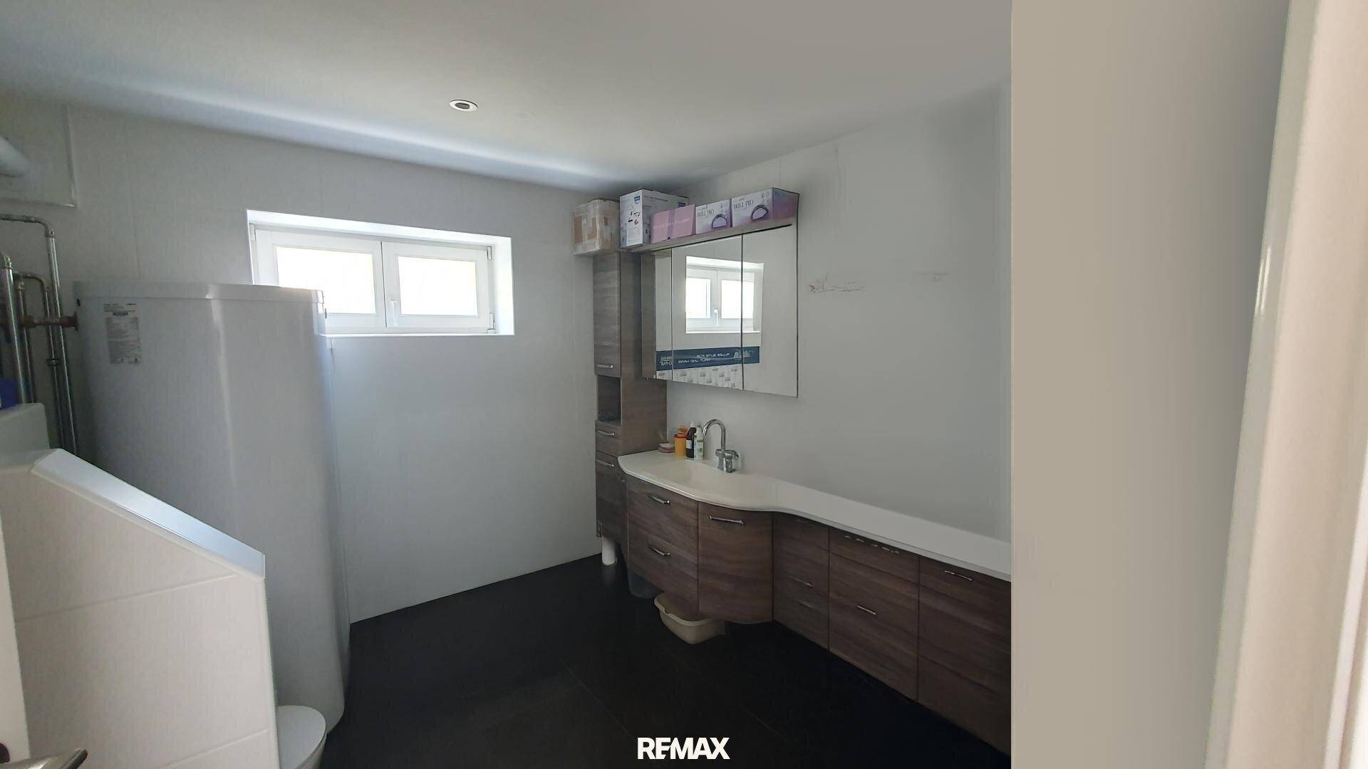Funktionaler Raum mit Toilette, Waschbecken, Spiegel und einem großen Warmwasserspeicher, ausgestattet mit Fenster.