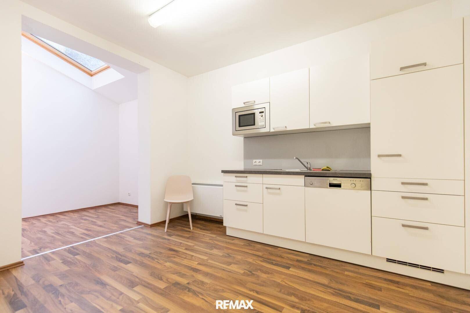 Moderne Küchenzeile mit weißen Schränken, Mikrowelle und Spülmaschine, angrenzend an einen Bereich mit Dachfenster.