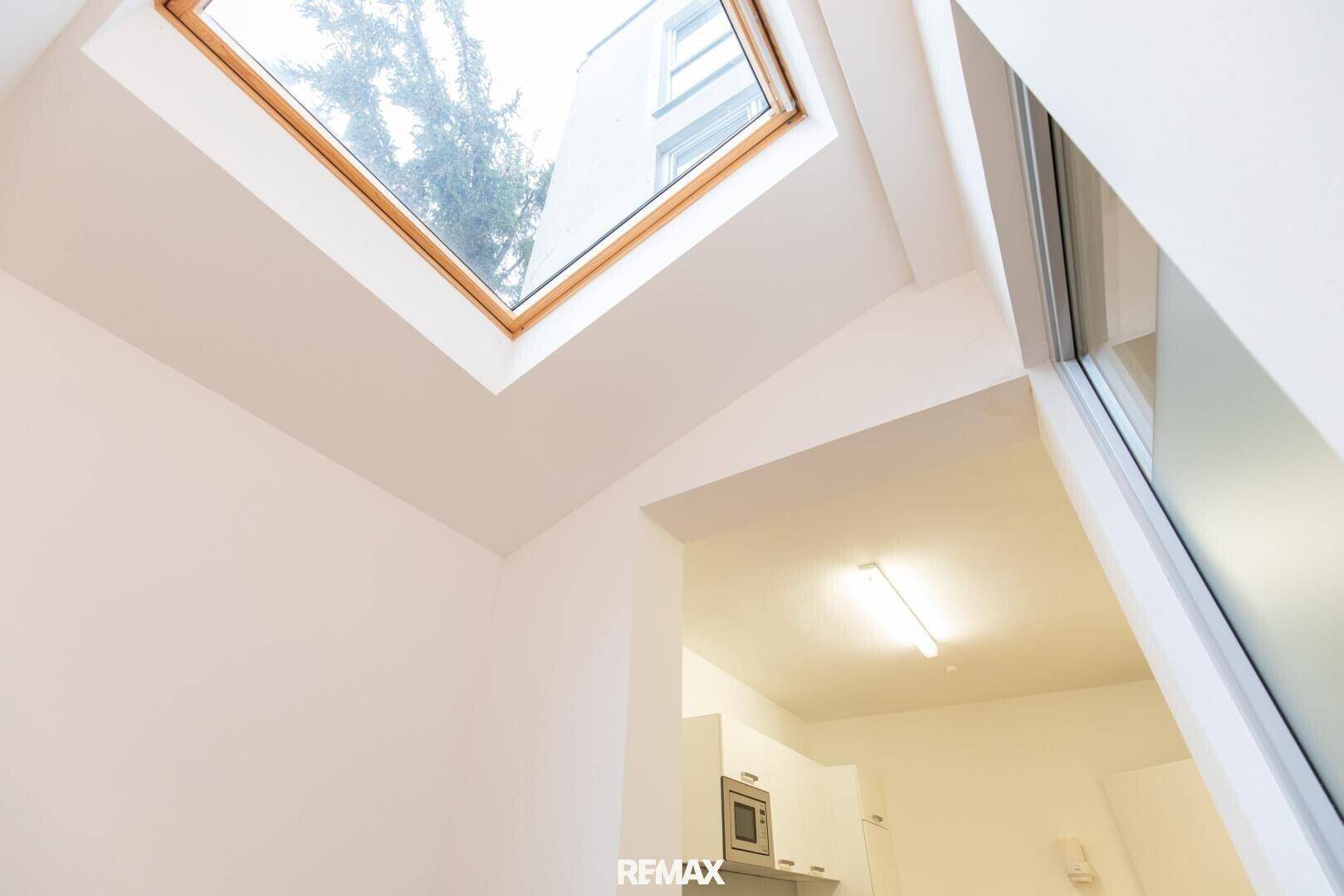 Großes Dachfenster lässt viel Tageslicht herein, mit Blick auf Bäume und den Himmel.