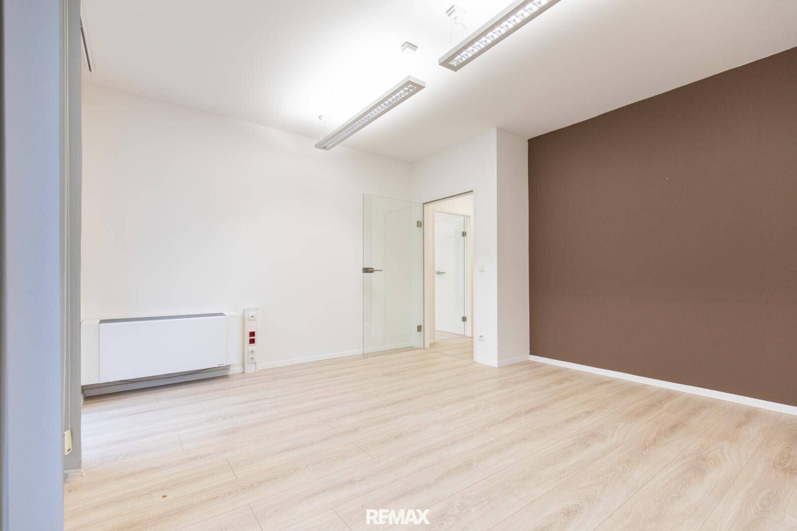 Büroraum mit hellem Laminatboden, weißen Wänden und einer braunen Akzentwand.