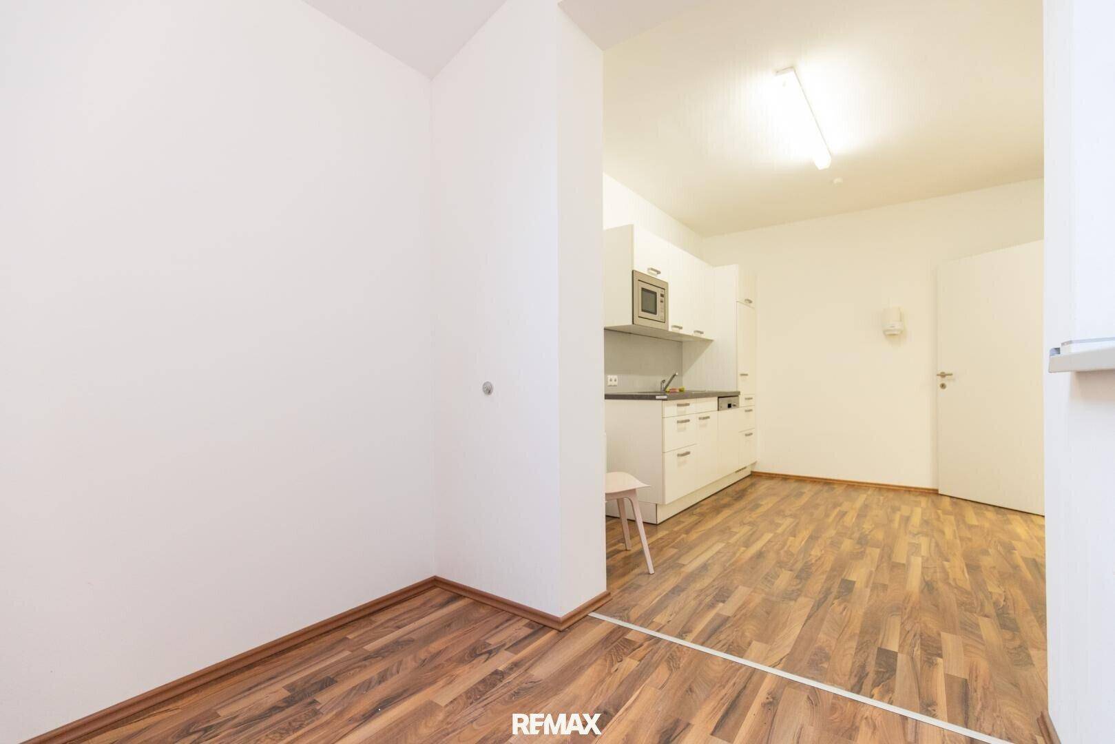 Küchenzeile mit weißen Schränken und dunklem Laminatboden in einem hellen, leeren Raum.