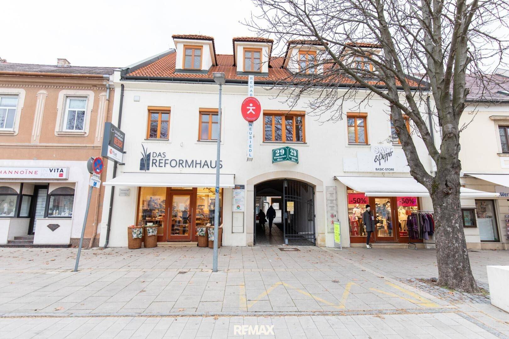 Historisches Gebäude mit Geschäften im Erdgeschoss und Wohnungen darüber, an einer belebten Straße gelegen.