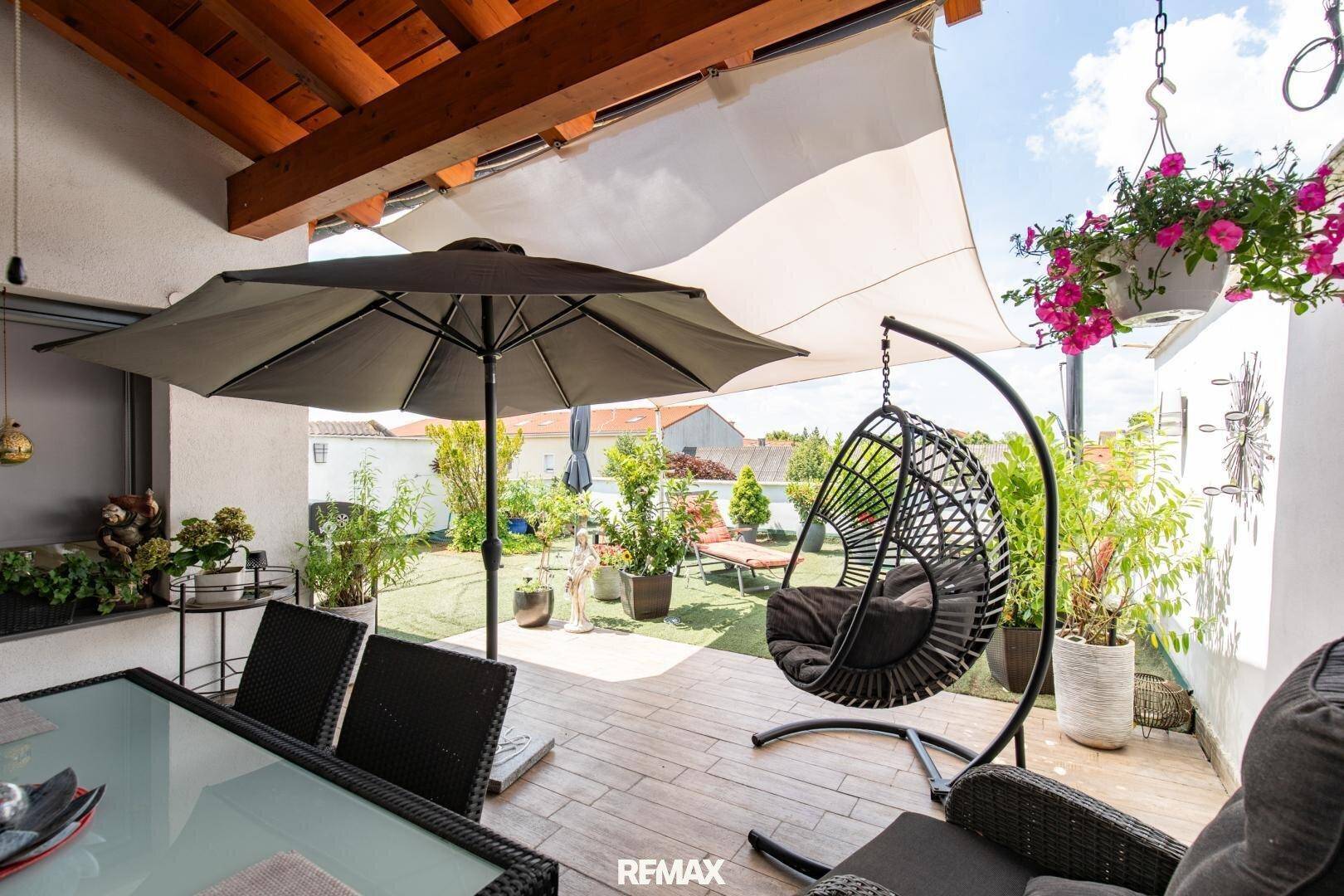 Gemütliche Terrasse mit Hängesessel, Esstisch und Sonnenschutz, umgeben von Pflanzen.