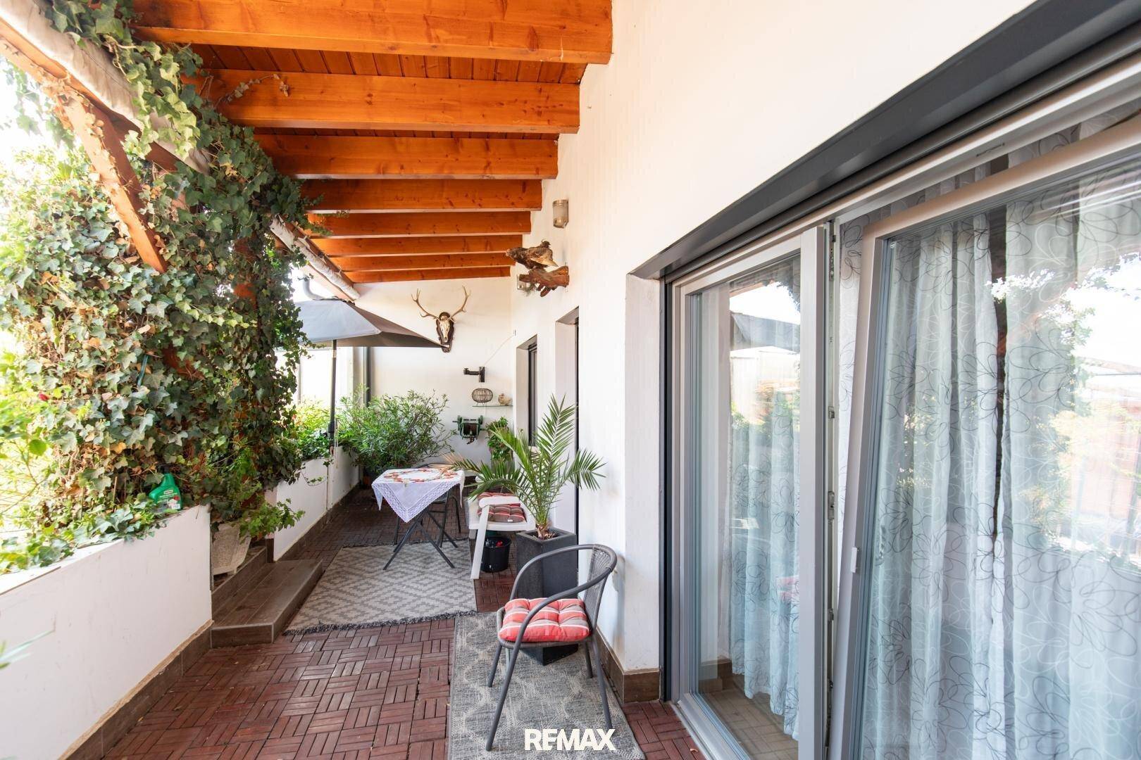 Überdachte Loggia mit Holzbalken, Sitzgelegenheiten und Pflanzen, ideal für entspannte Stunden.