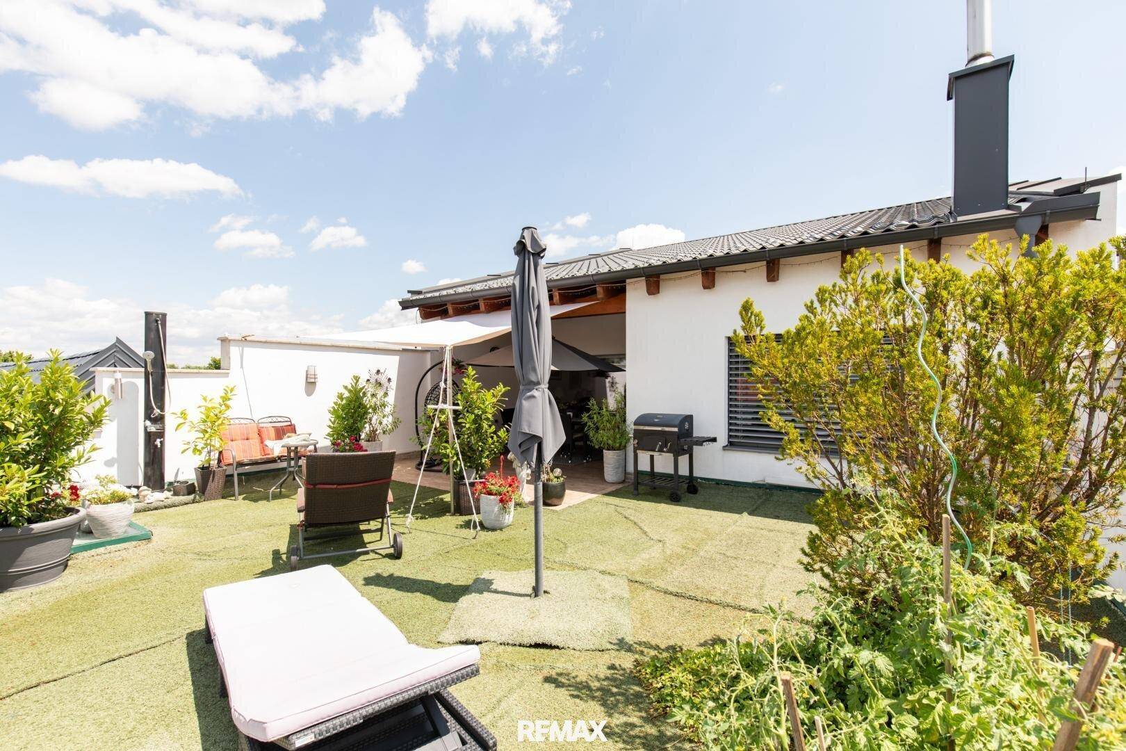Weitläufige Dachterrasse mit Kunstrasen, Sonnenliegen und Blick auf die Umgebung, sehr sonnig.