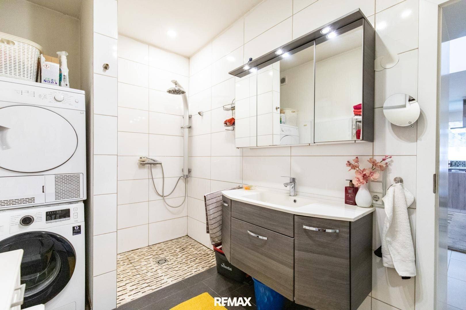 Modernes Badezimmer mit Dusche, Waschbecken und integrierter Waschmaschine und Trockner.