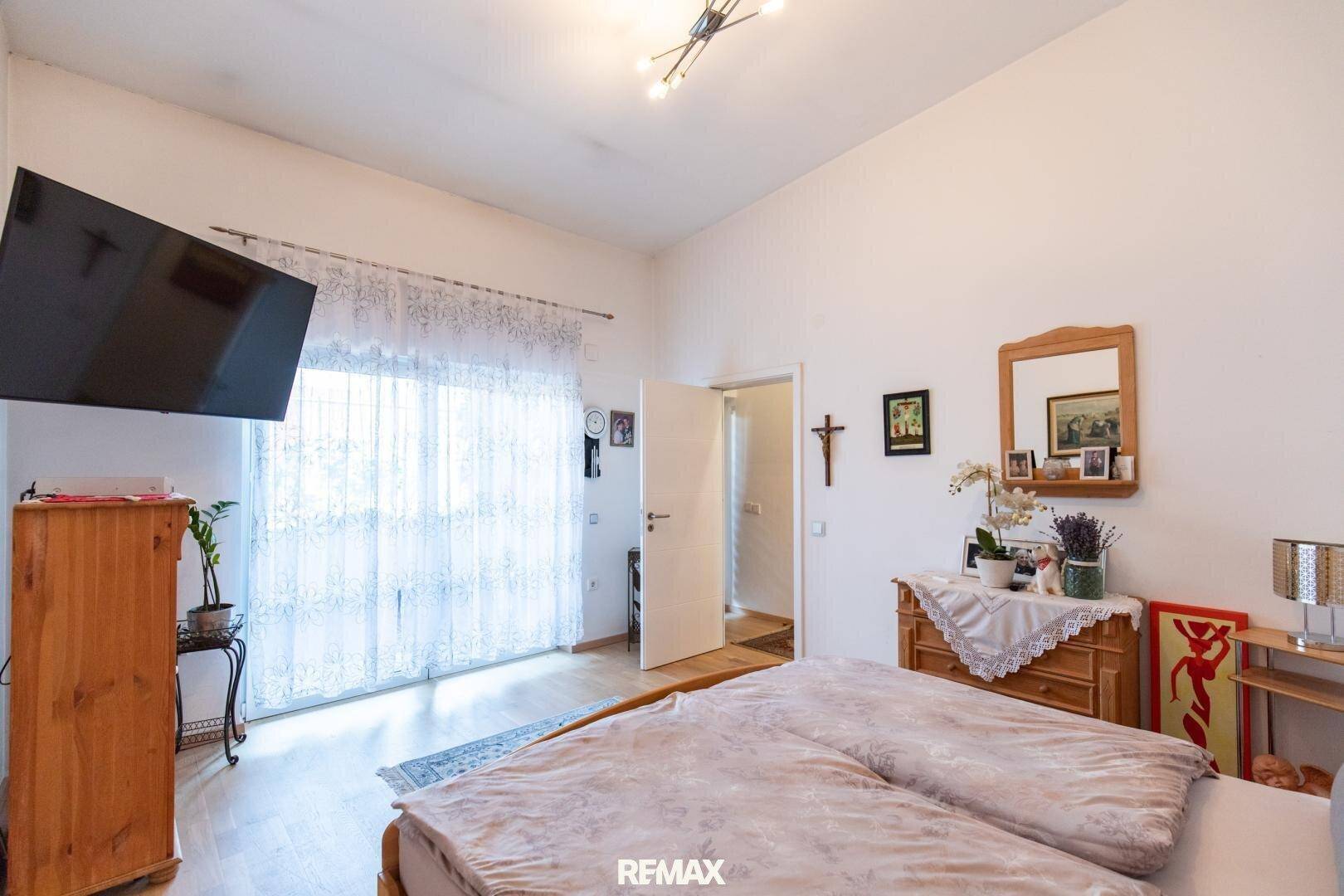 Helles Schlafzimmer mit Holzboden und großem Fenster, bietet direkten Zugang zum Außenbereich.
