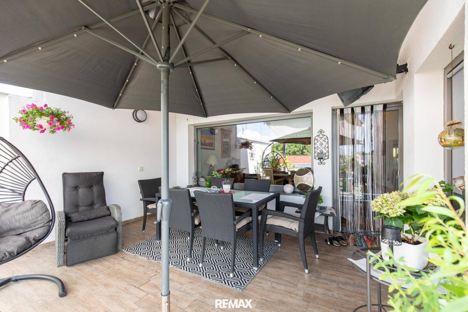 Überdachter Terrassenbereich mit Esstisch und Hängesessel, bietet Schutz vor Sonne und Regen.