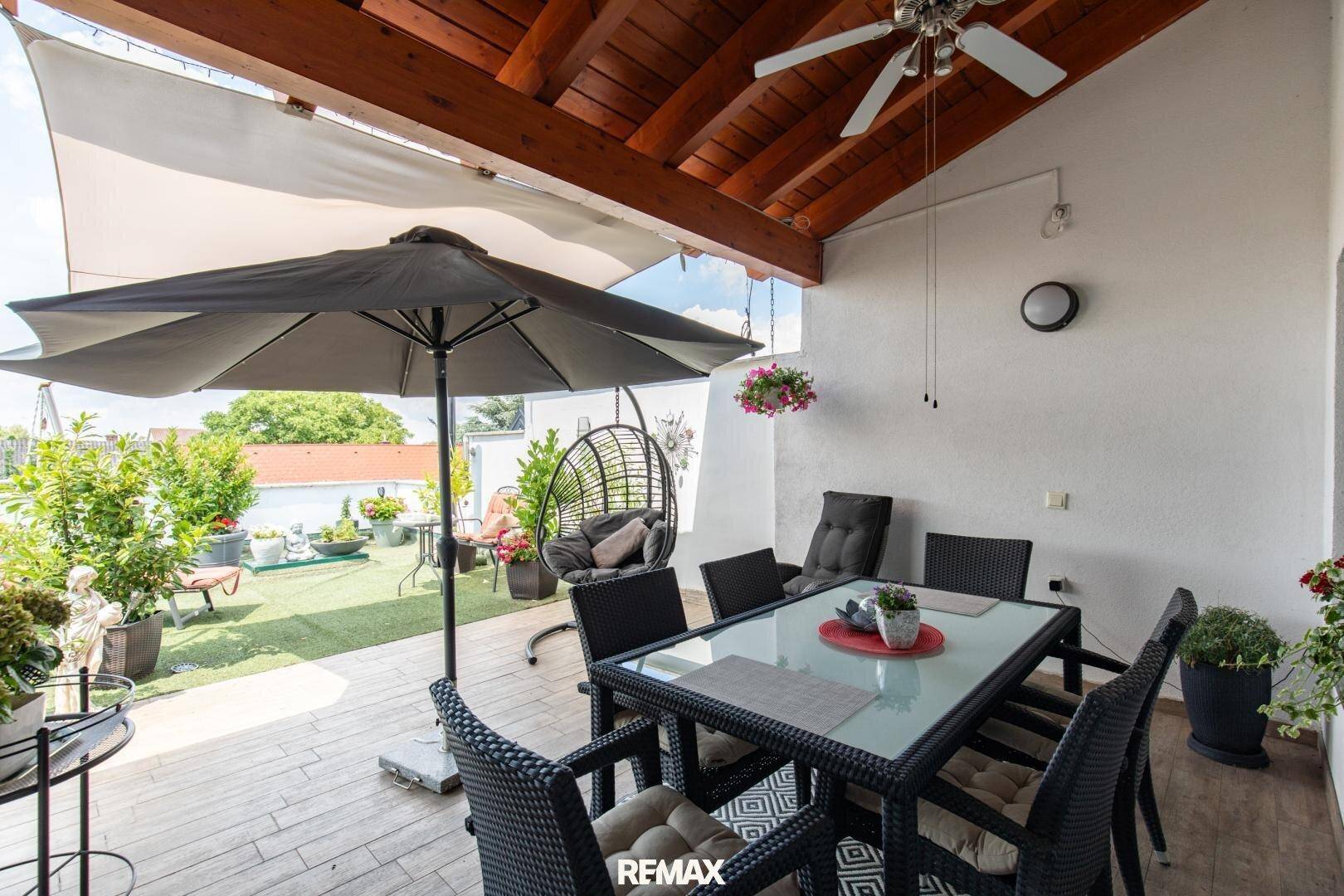 Überdachte Terrasse mit Esstisch, Deckenventilator und Blick auf den Garten, ideal für Mahlzeiten im Freien.