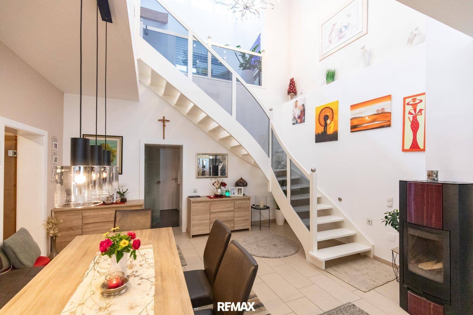 Heller Wohn-Essbereich mit Kaminofen, offener Treppe und hohen Decken, modern eingerichtet.