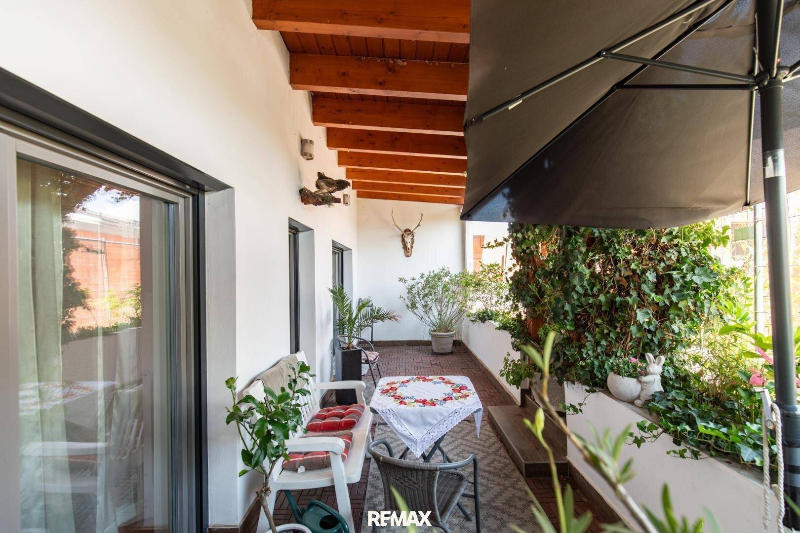 Gemütliche Loggia mit Esstisch, Sonnenschirm und üppiger Begrünung, lädt zum Verweilen ein.