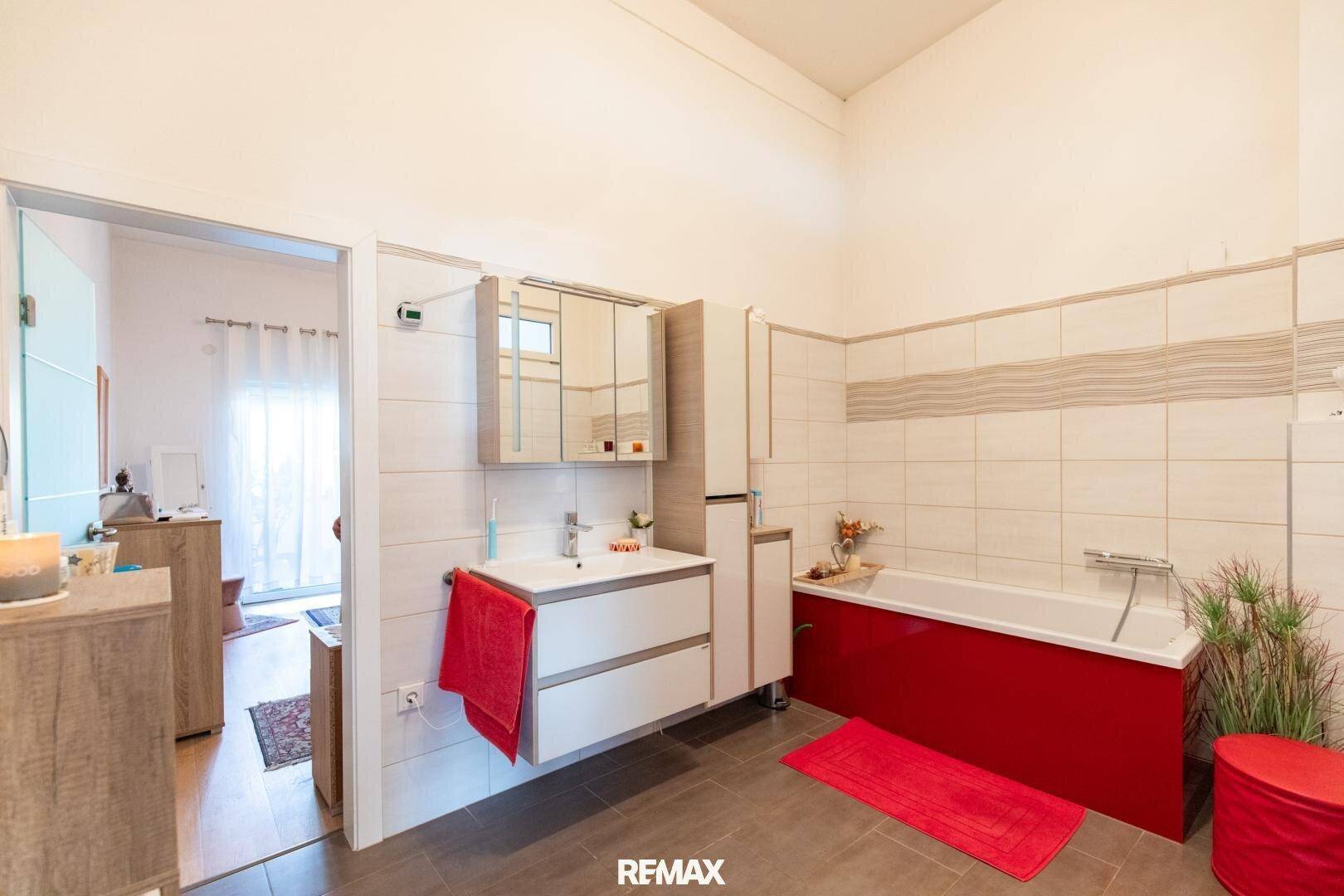 Geräumiges Badezimmer mit Badewanne, Waschbecken und Fliesenboden, in hellen Farben gehalten.
