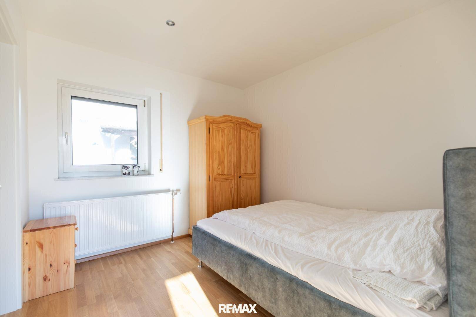 Schlafzimmer mit Bett, Holzschrank und hellem Laminatboden, gut beleuchtet.
