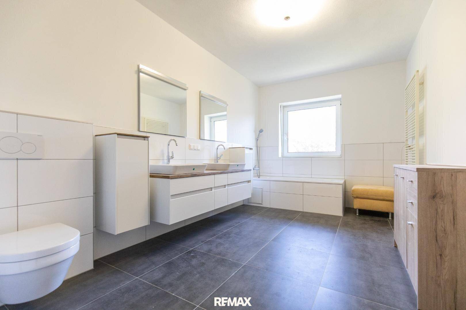 Modernes Badezimmer mit Doppelwaschbecken, Badewanne und großformatigen Fliesen.