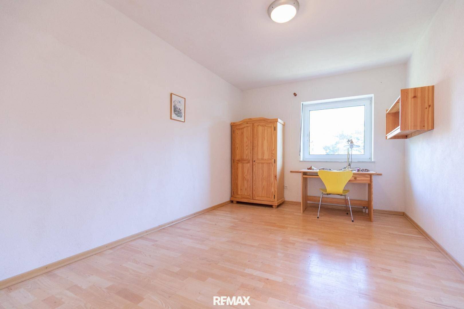 Helles Zimmer mit Holzboden, Schreibtisch und Schrank, ideal als Büro oder Kinderzimmer.