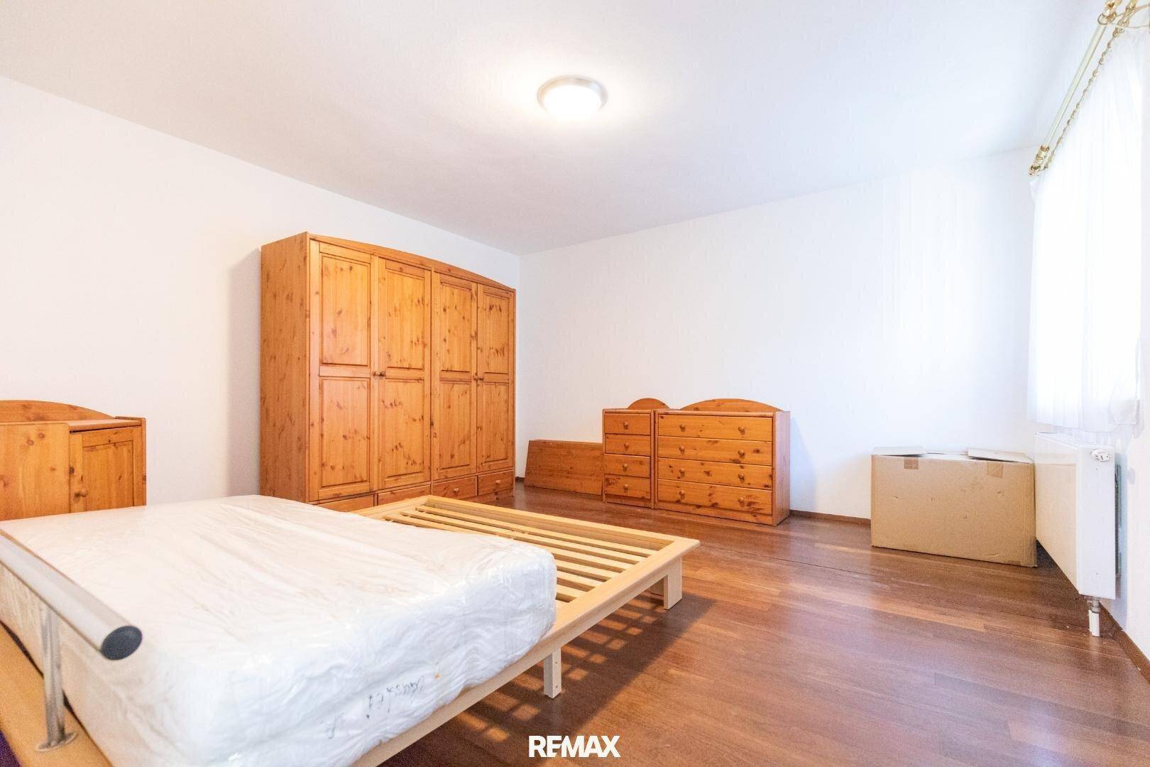 Geräumiges Schlafzimmer mit Holzmöbeln, dunklem Parkettboden und viel Tageslicht.