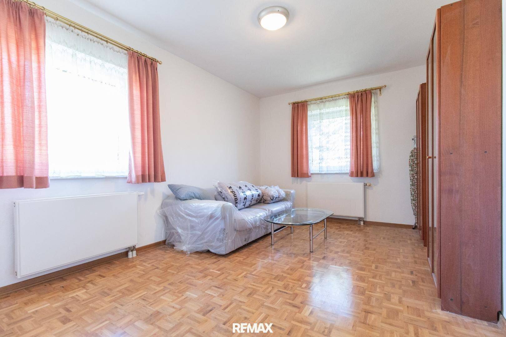 Gemütlicher Raum mit Parkettboden, Sofa und Vorhängen, ideal als Gäste- oder Wohnzimmer.
