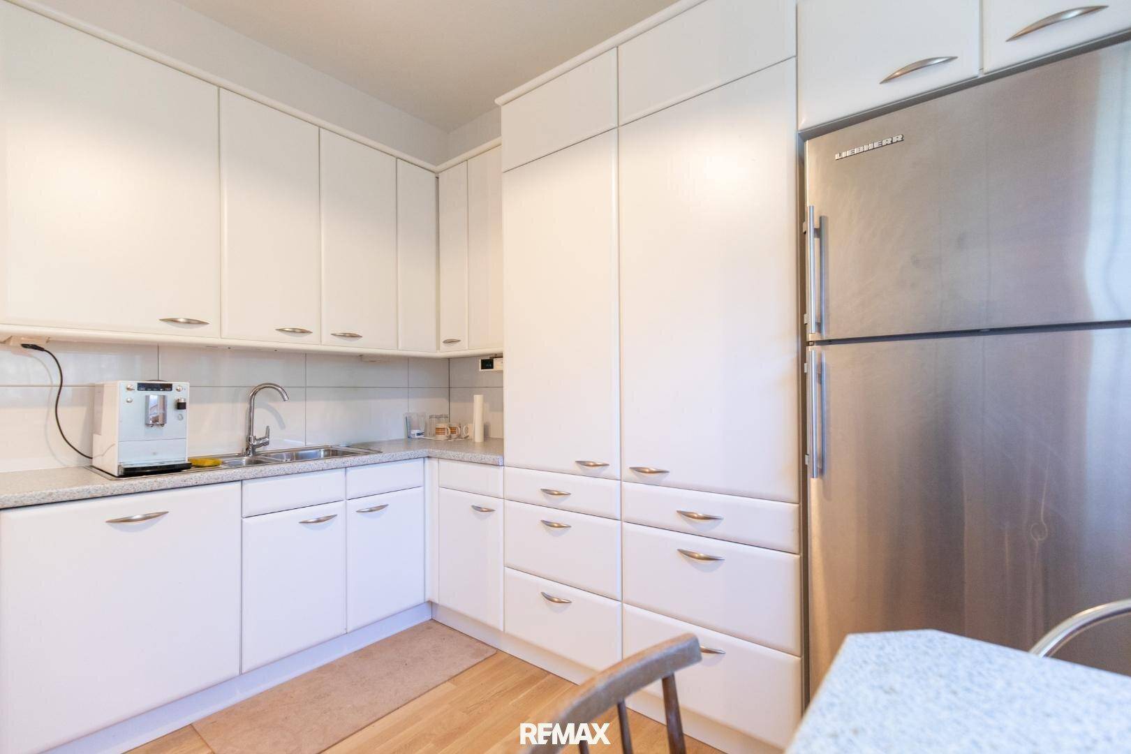 Funktionale Küche mit weißen Schränken, Edelstahlkühlschrank und heller Arbeitsplatte.