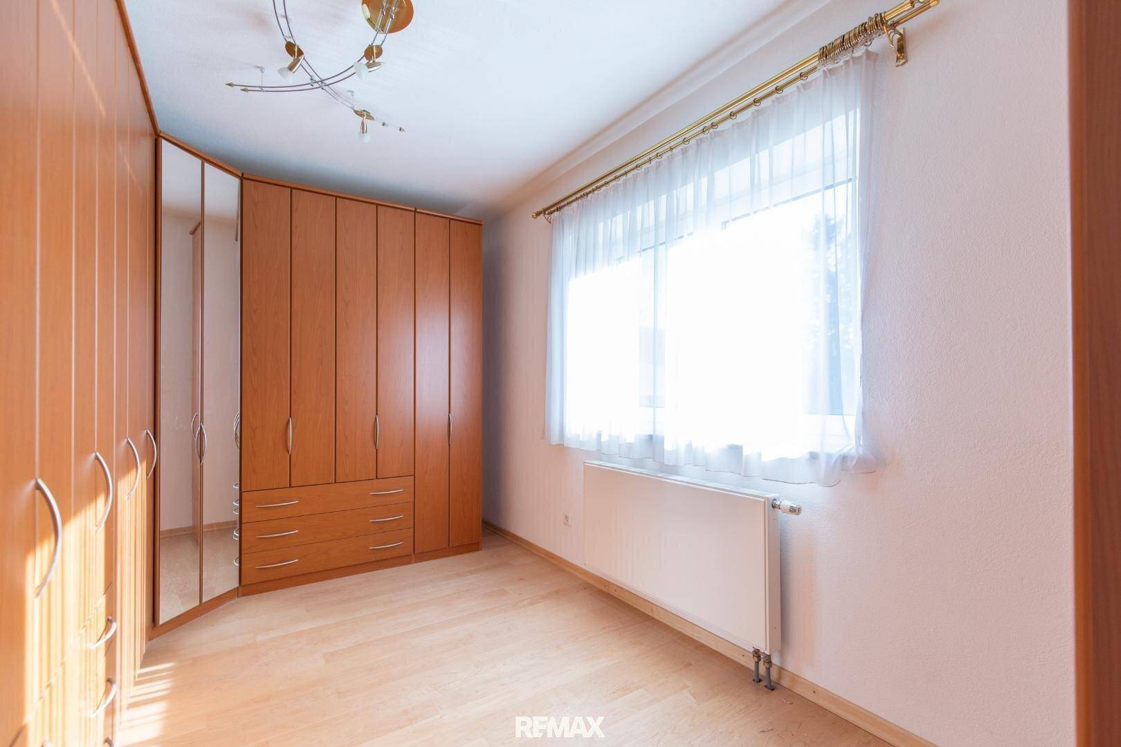 Schlafzimmer mit großen Holzschränken, hellem Boden und Fenster mit Vorhängen.