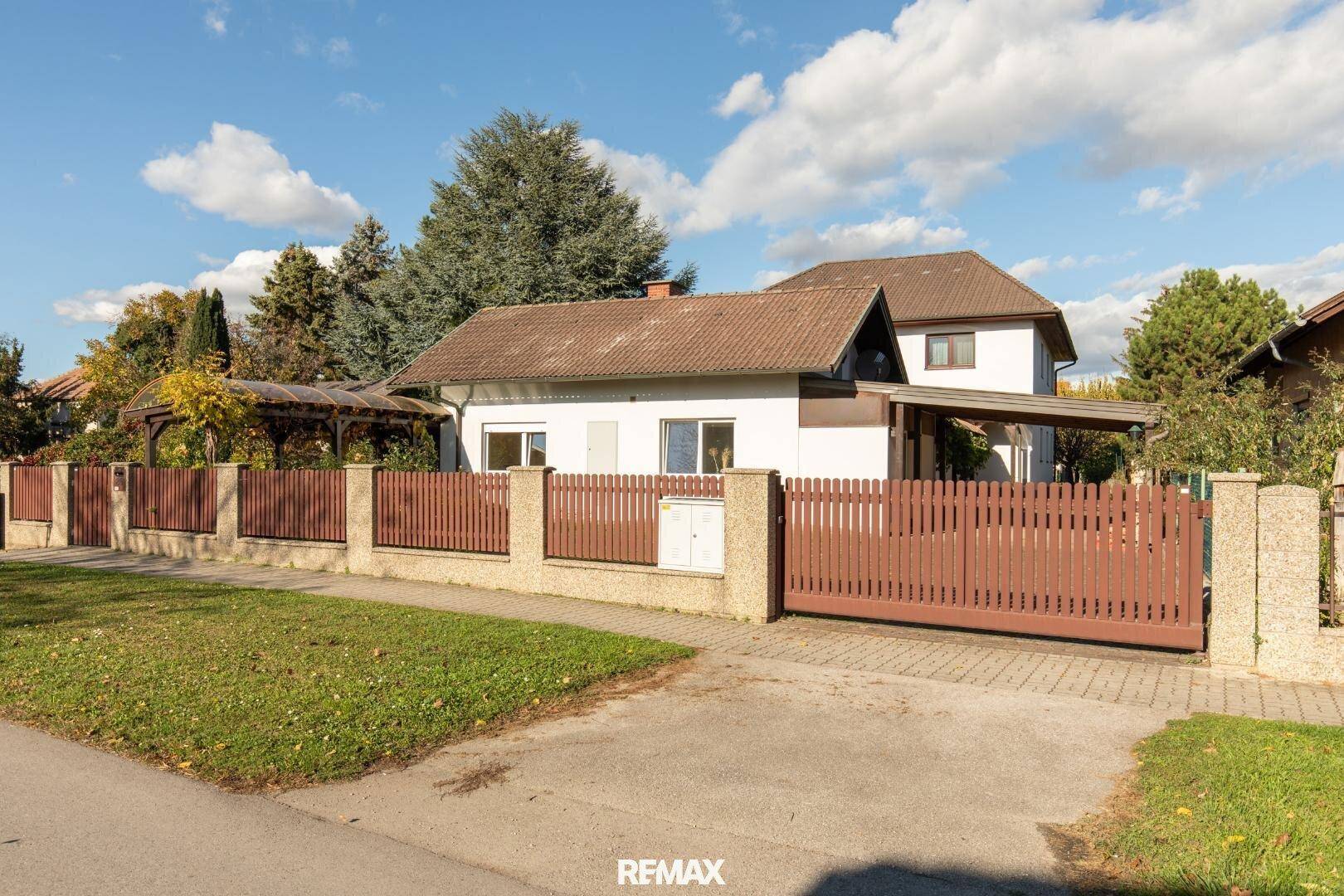 Ansicht des Hauses von der Straße mit Holzzaun, Einfahrt und Carport.
