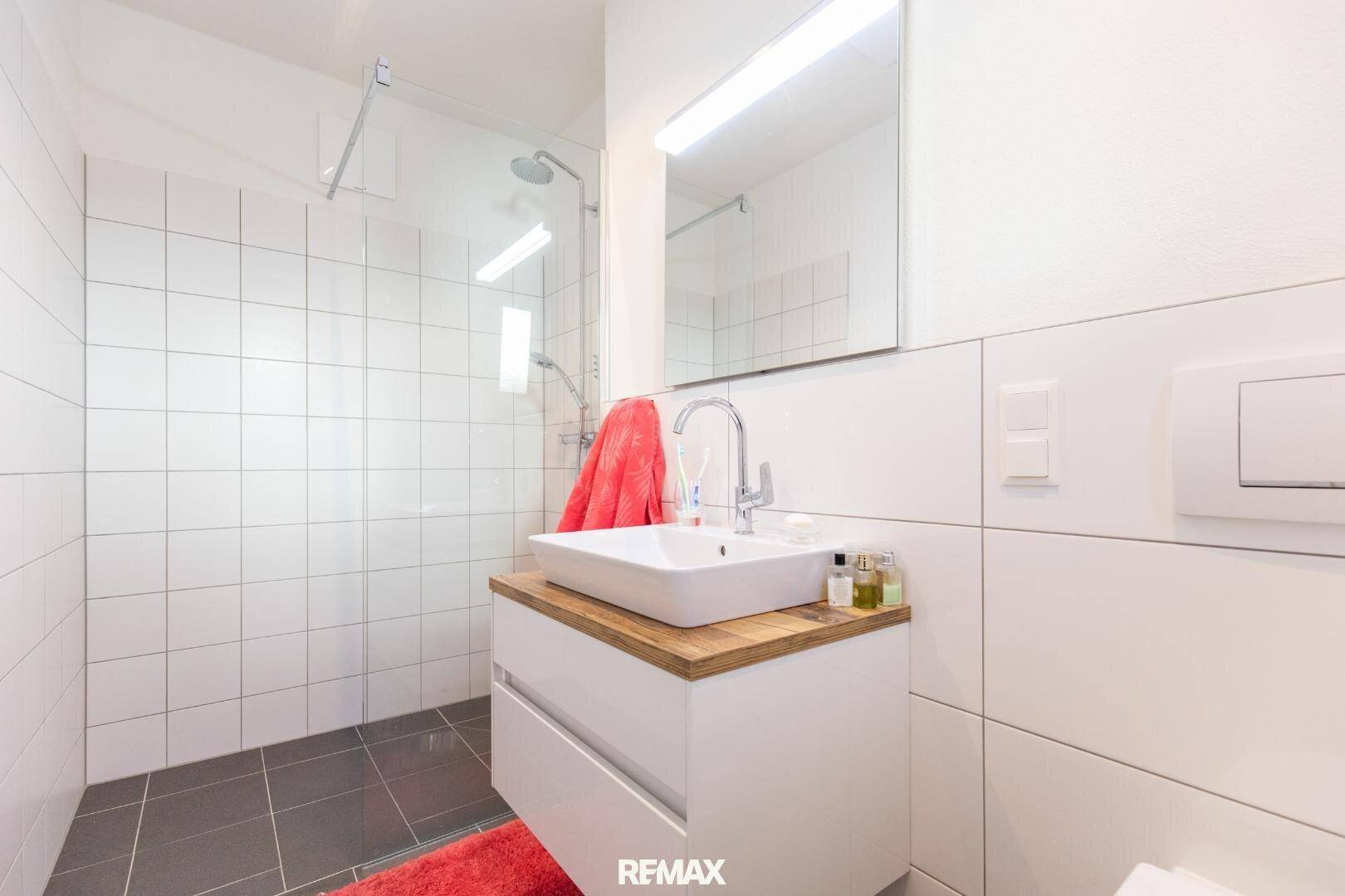 Modernes Badezimmer mit Dusche, Waschtisch und weißen Fliesen, gut beleuchtet.