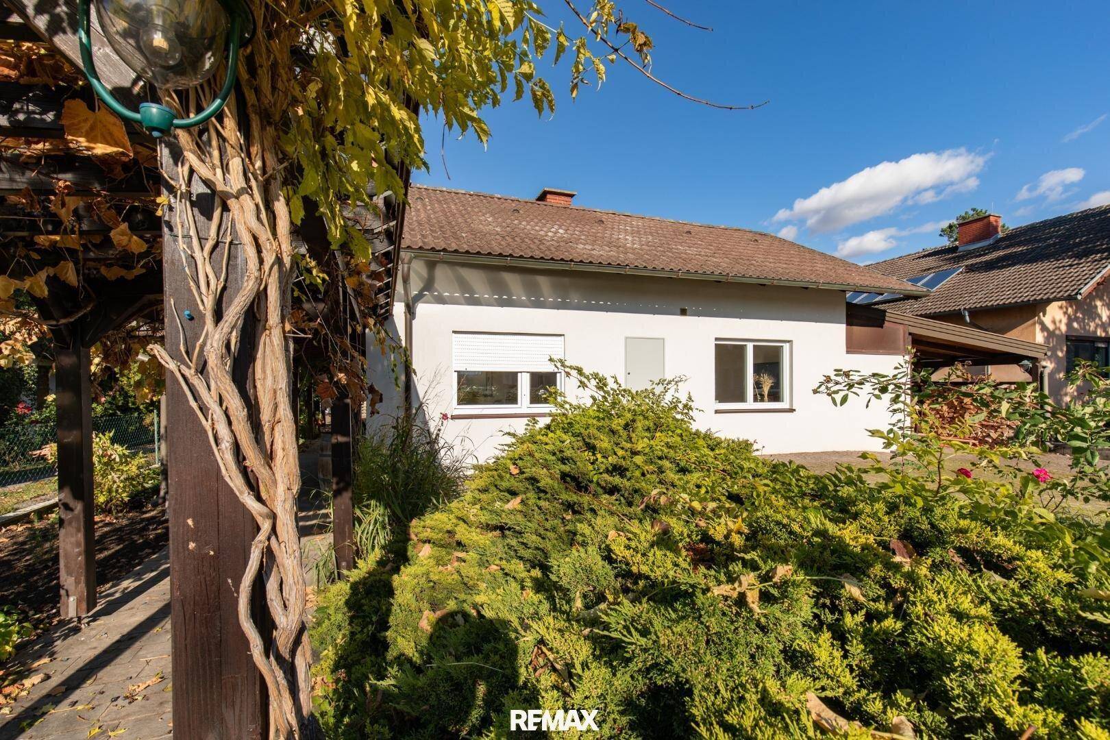 Seitenansicht des Hauses mit grüner Hecke im Vordergrund und Rollläden an den Fenstern.