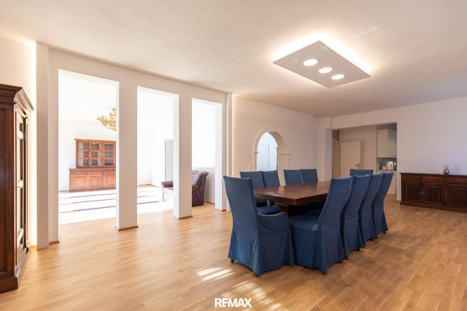 Geräumiger Essbereich mit großem Holztisch und blauen Stühlen, offen zum Wohnzimmer.