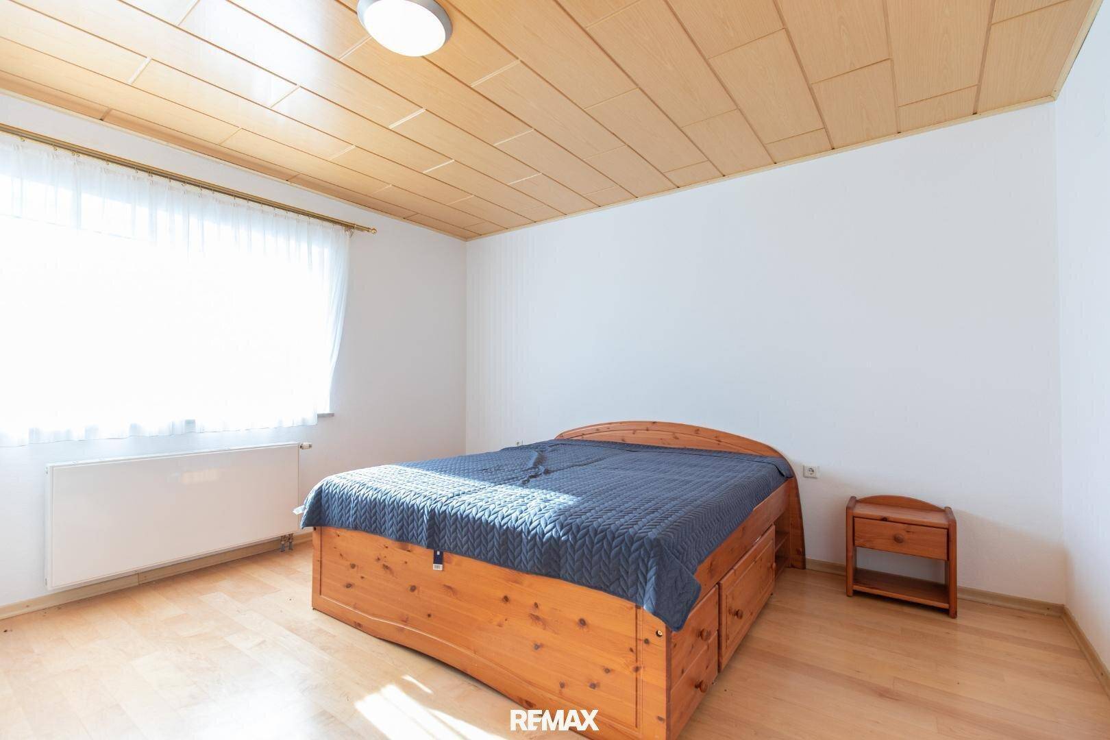 Schlafzimmer mit Holzbett, Holzdecke und hellem Laminatboden, gut beleuchtet.