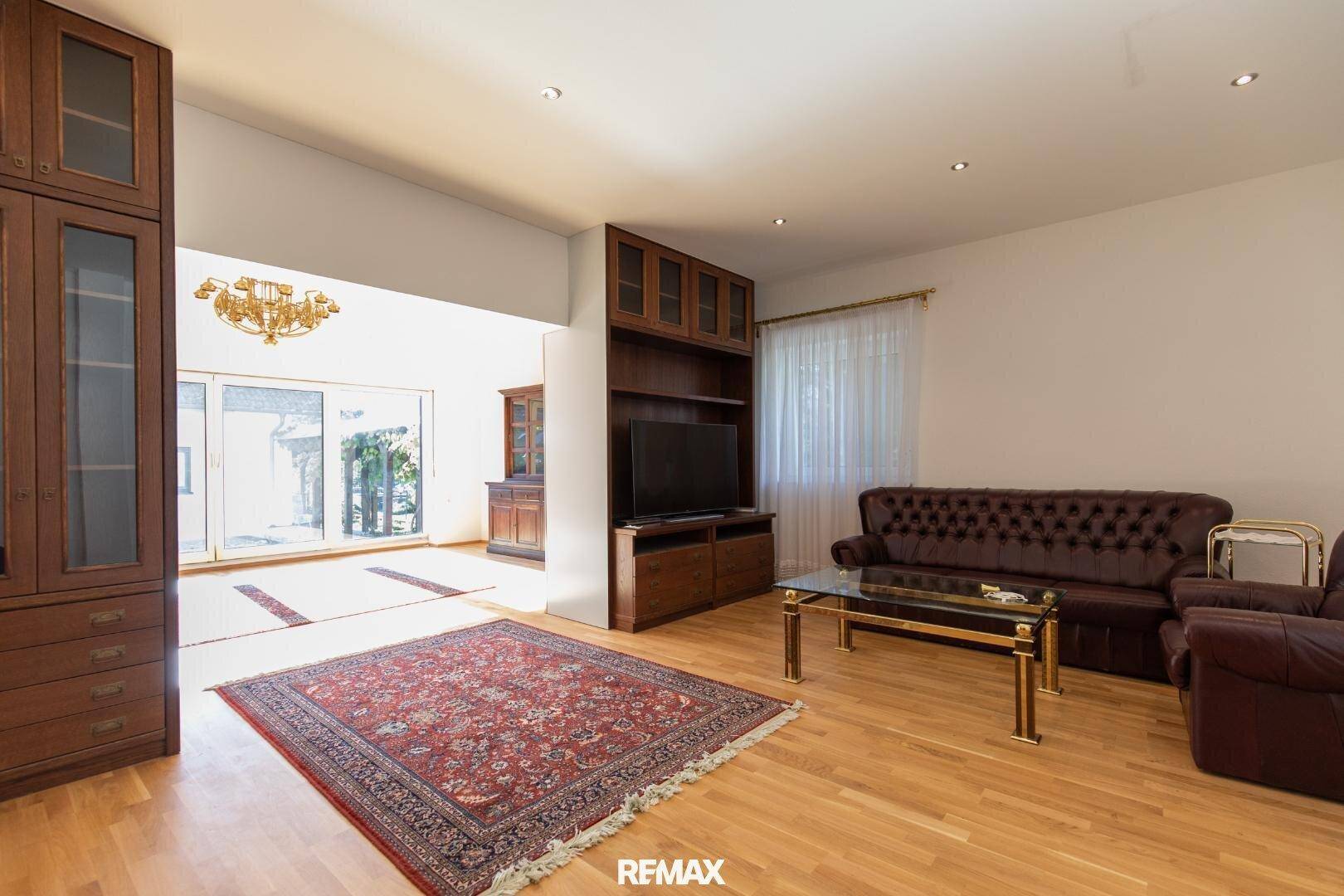 Gemütliches Wohnzimmer mit Holzeinbauschränken, Ledersofa und Blick in den angrenzenden Bereich.