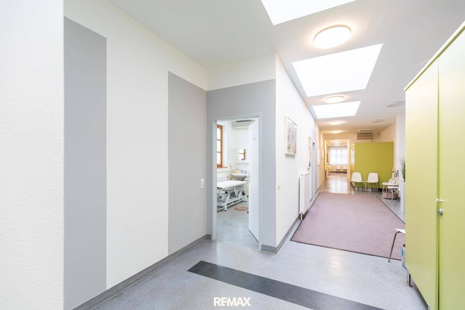 Heller Flur mit Zugang zu mehreren Behandlungsräumen, ausgestattet mit modernen Leuchten und sauberem Boden.