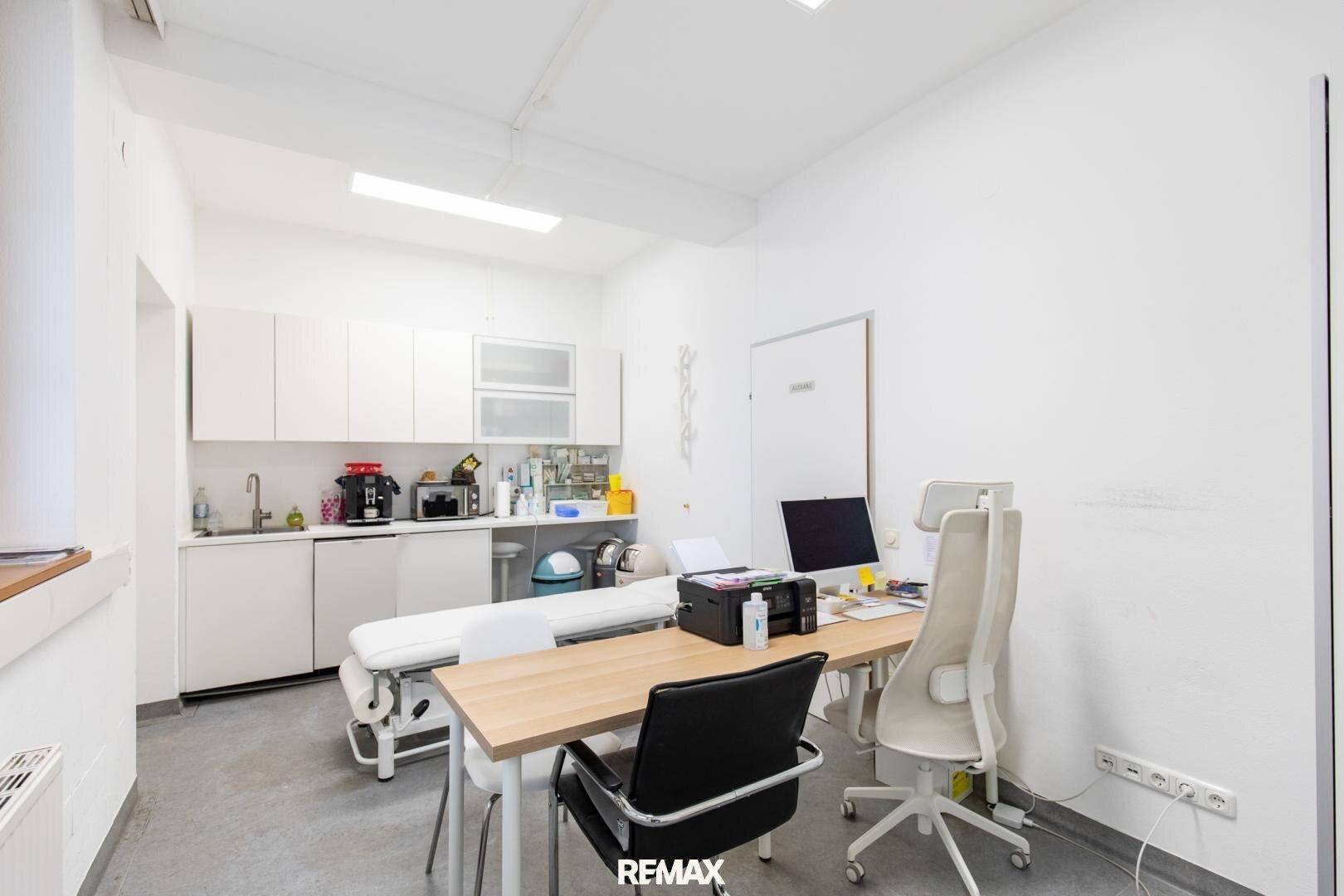 Untersuchungszimmer mit integrierter Küchenzeile, Schreibtisch und Behandlungsliege, praktisch und hell gestaltet.