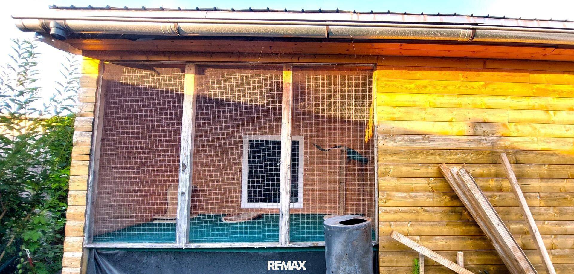 Detailansicht eines Holzschuppens mit vergittertem Fenster und Holzverkleidung an der Fassade.