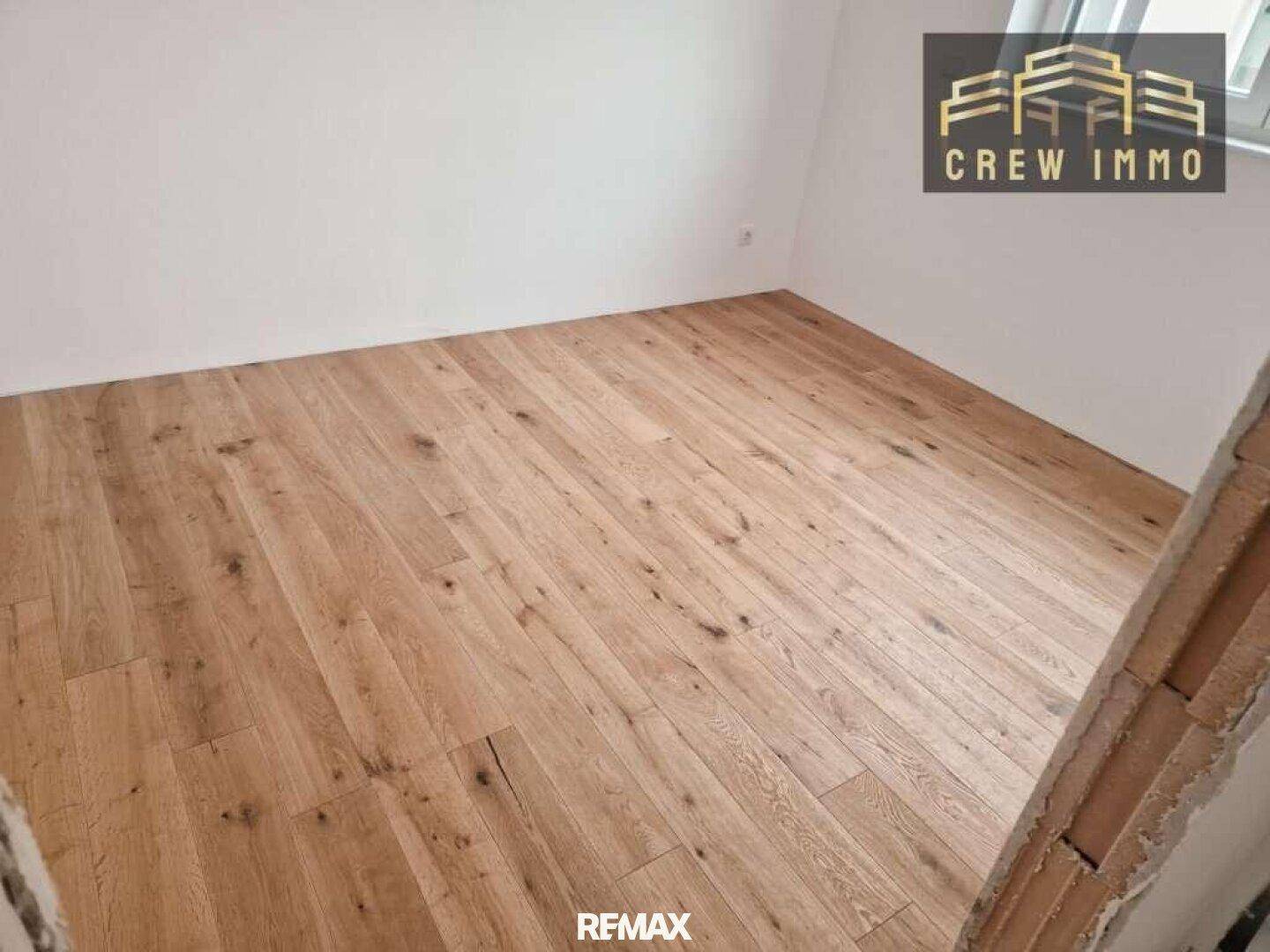 Heller Raum mit neu verlegtem Holzfußboden und weißen Wänden, ideal für ein Schlafzimmer.