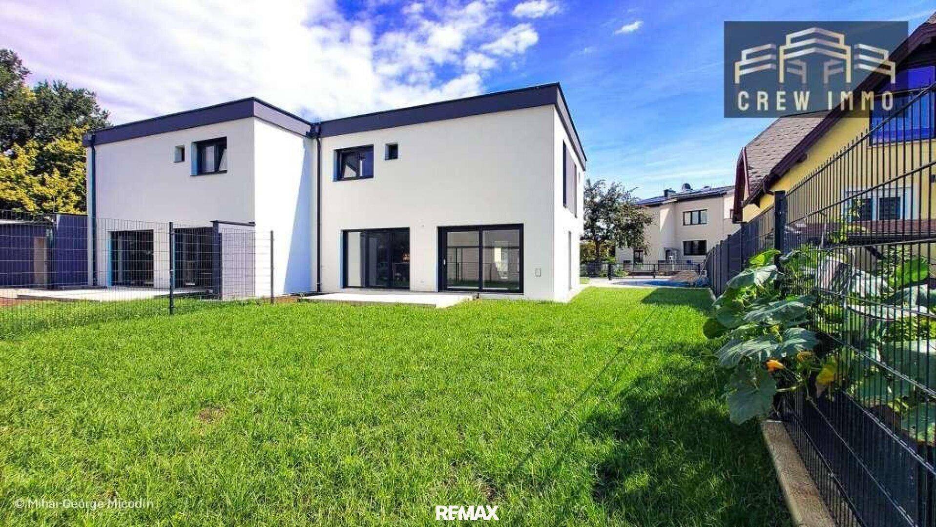 Hinteransicht des modernen Hauses mit großem Rasenbereich und bodentiefen Fenstern zum Garten.