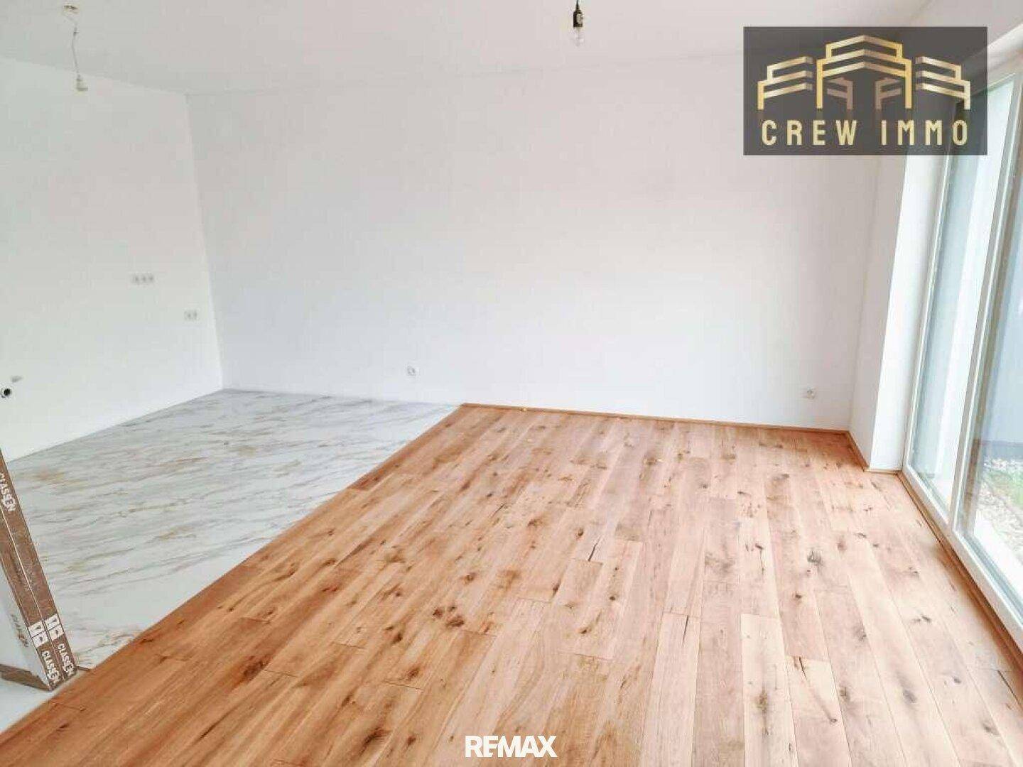 Geräumiger Raum mit teilweise verlegtem Holz- und Fliesenboden, großen Fenstern und viel Tageslicht.