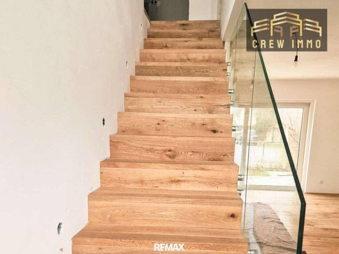 Elegante Holztreppe mit Glasbrüstung in einem modernen Haus, das noch im Bau ist.