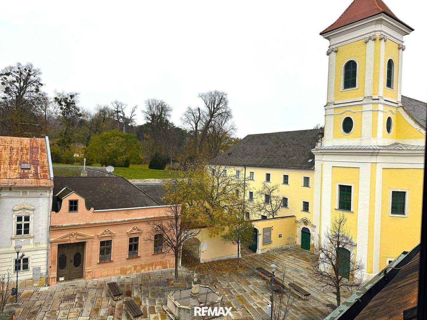 Historischer Innenhof mit Kopfsteinpflaster, Brunnen und angrenzender Kirche.