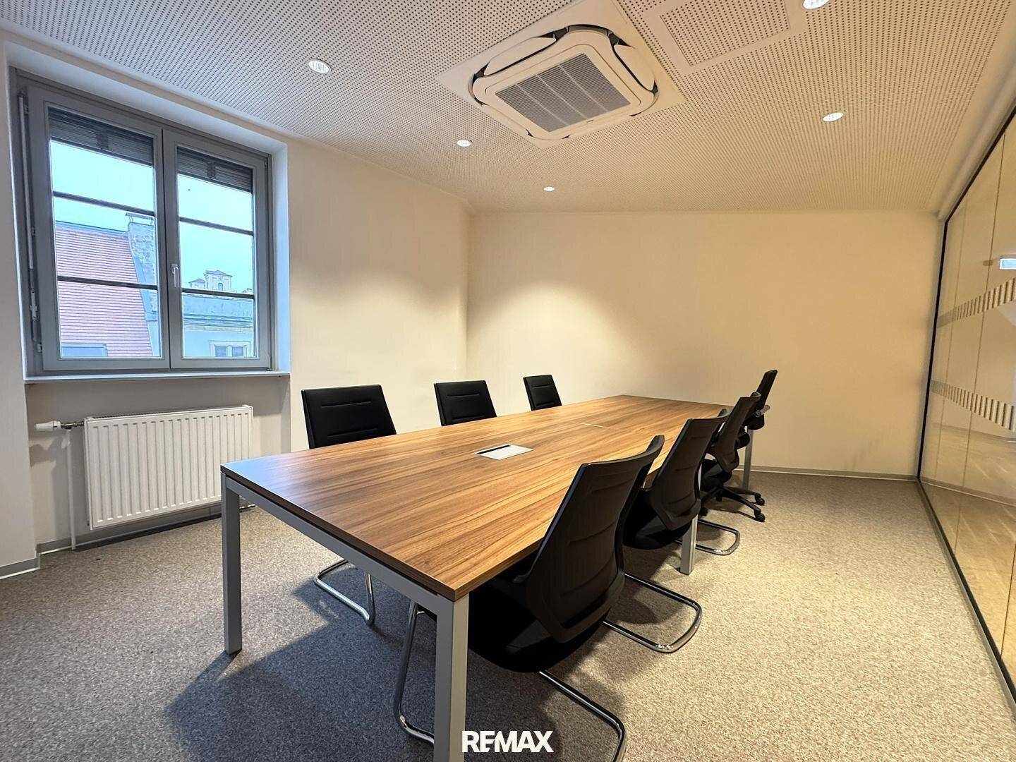 Konferenzraum mit großem Holztisch, Bürostühlen und Teppichboden.