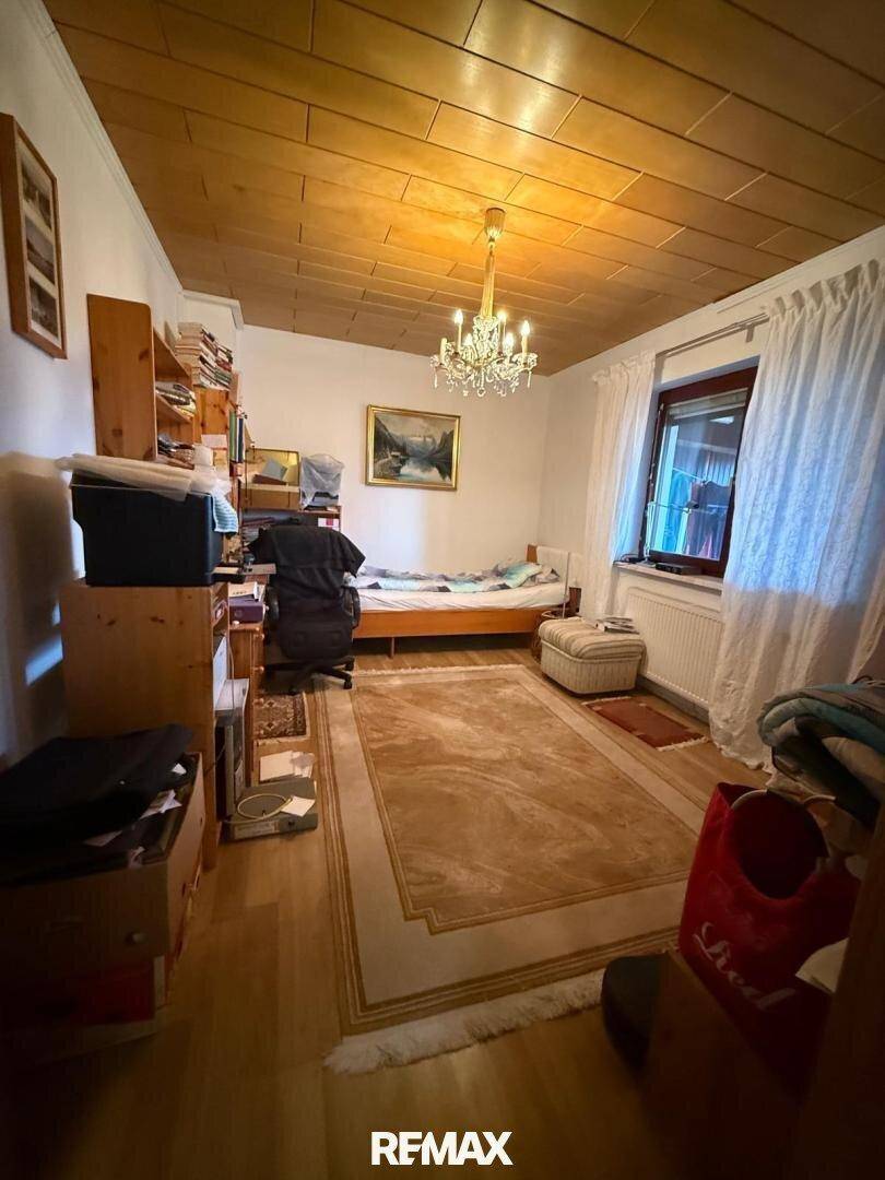 Gemütliches Schlafzimmer mit Holzbalkendecke, Parkettboden, Teppich und Schreibtischbereich.