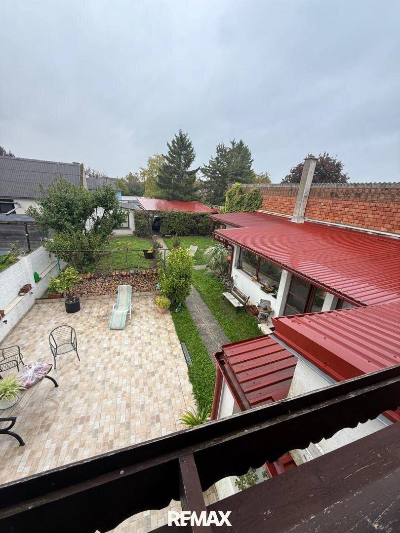 Blick von oben auf den Gartenbereich mit gepflasterter Terrasse und rotem Dach.