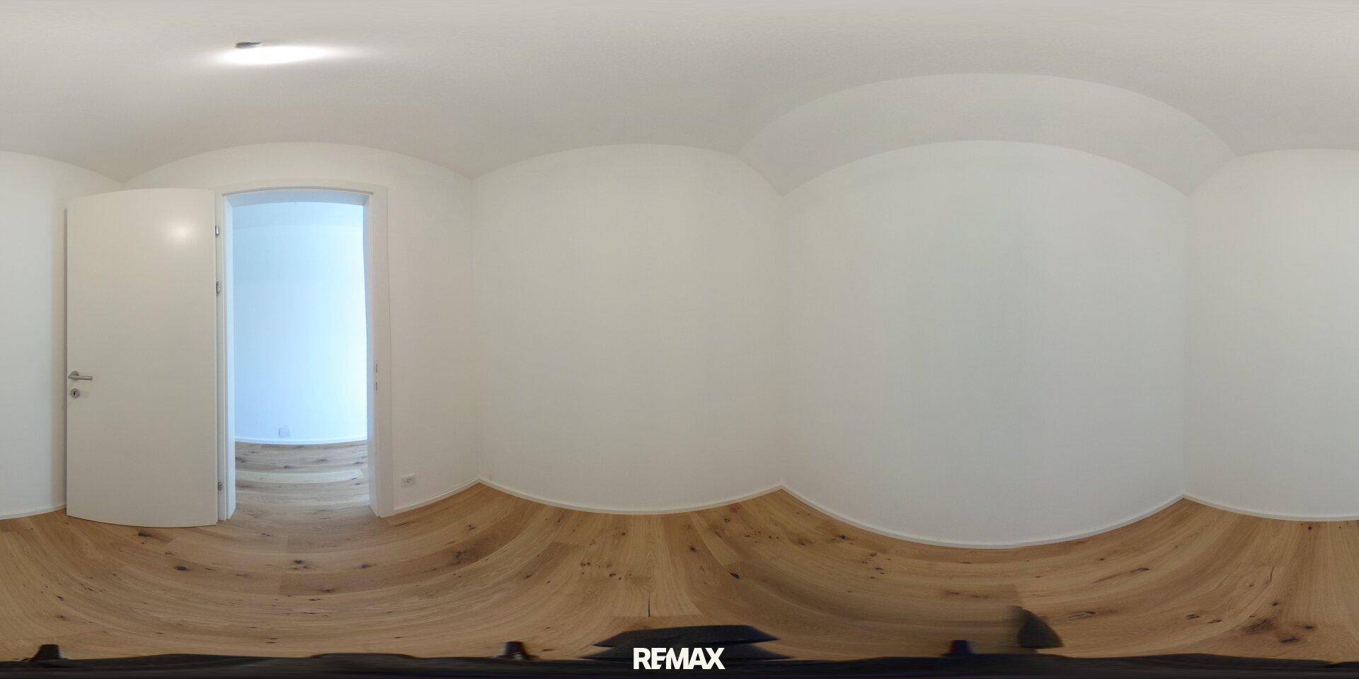 Leerer Raum mit hellen Wänden und Holzboden, der durch eine Tür in einen weiteren Raum führt.