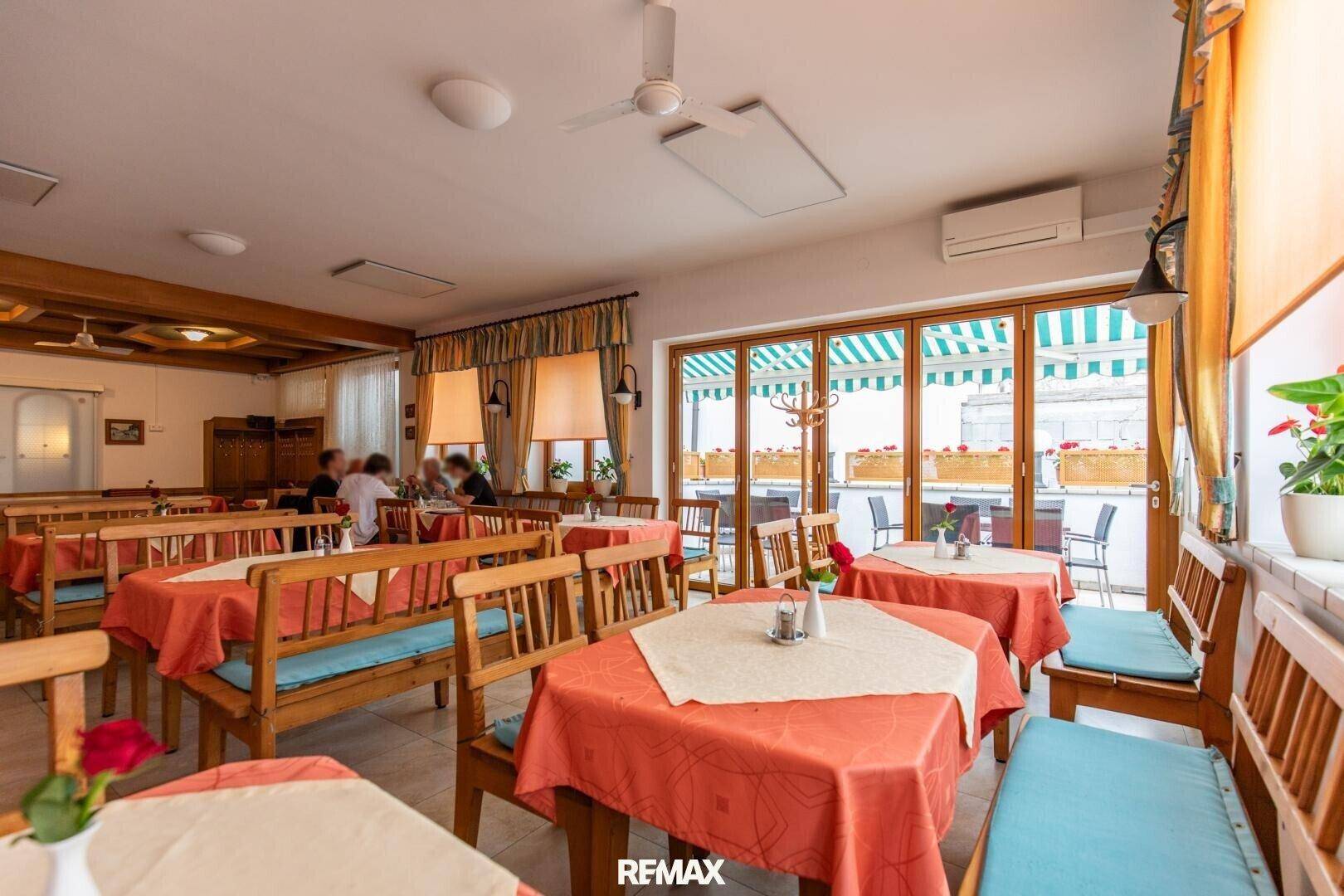 Heller Restaurantbereich mit Holztischen und Bänken, Klimaanlage und großen Fenstern zum Außenbereich.
