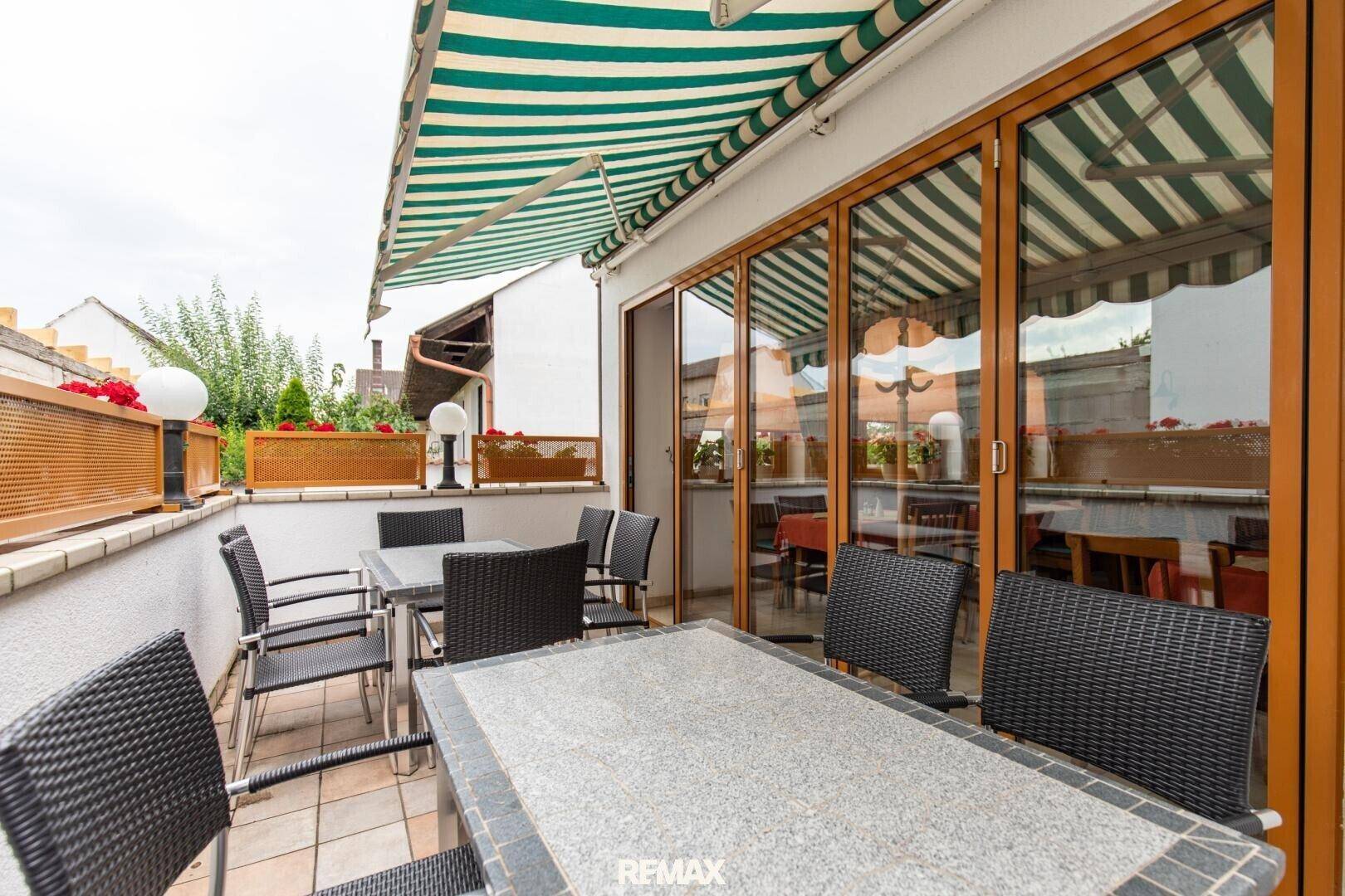 Überdachte Terrasse mit Esstischen und Stühlen, geschützt durch eine Markise, mit Zugang zum Innenbereich.