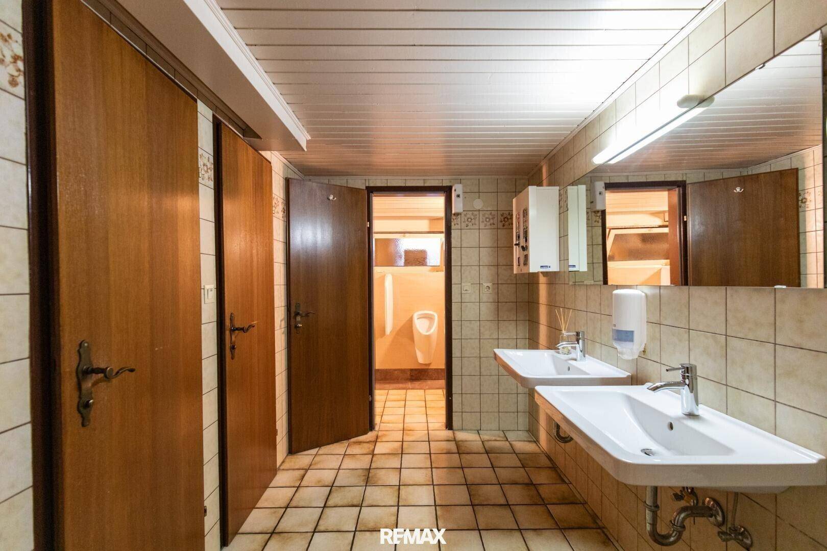Geräumiger öffentlicher Waschraum mit mehreren Waschbecken, großen Spiegeln und gefliesten Wänden und Böden.
