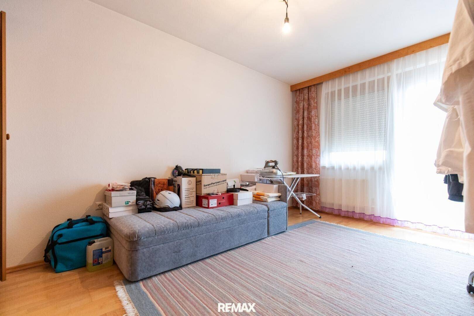 Helles Schlafzimmer oder Mehrzweckraum mit Holzboden, großem Fenster und Vorhängen.
