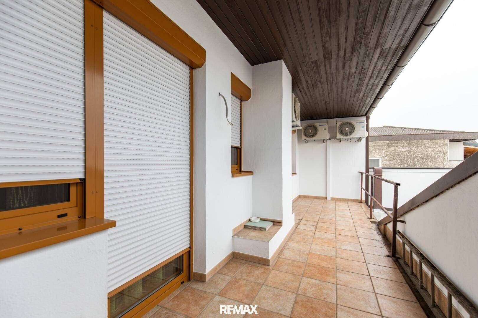 Geräumiger Balkon mit Fliesenboden, Rollläden an den Fenstern und externen Klimaanlagen.