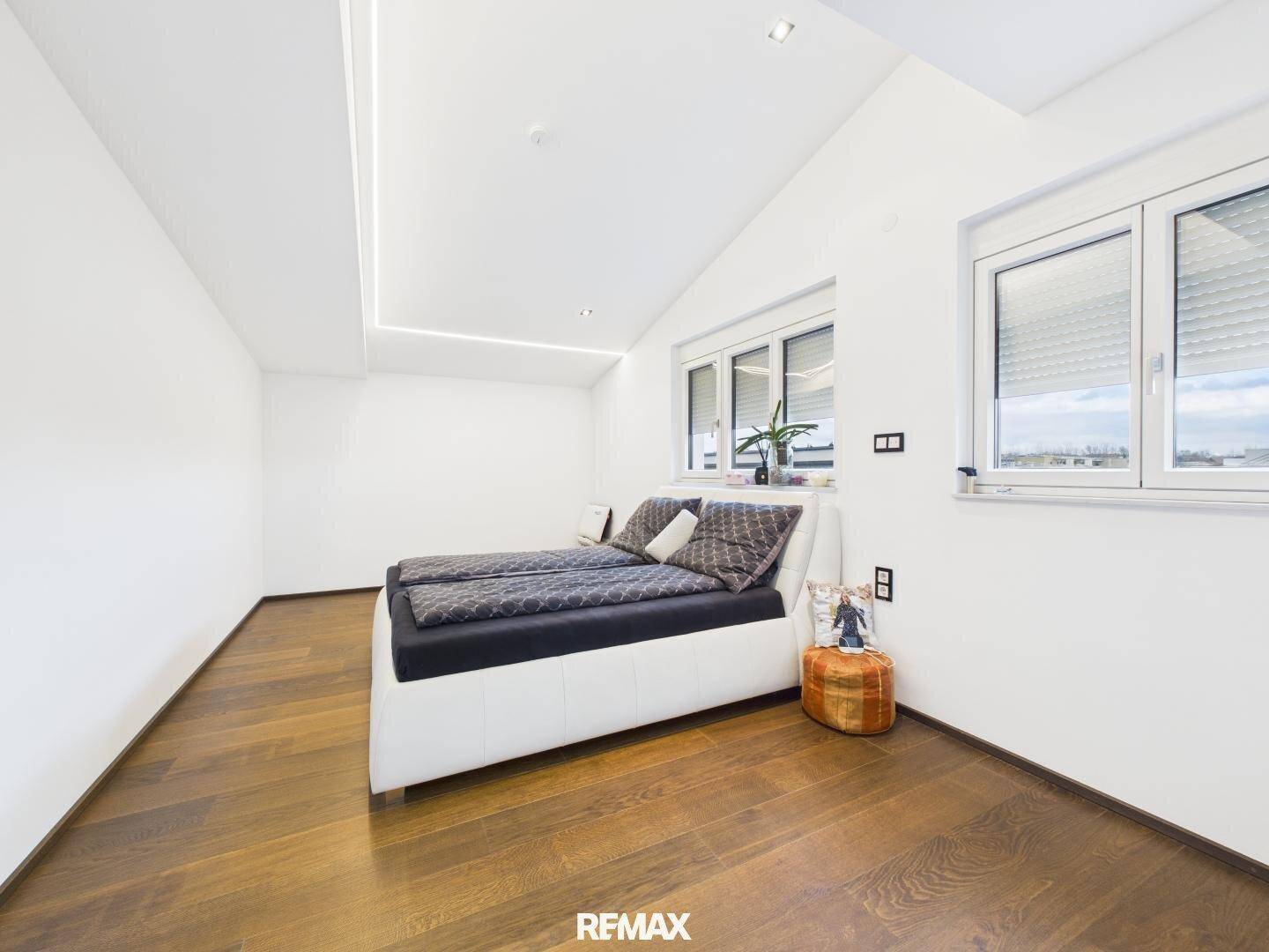 Helles Schlafzimmer mit Holzboden, Doppelbett und großen Fenstern.