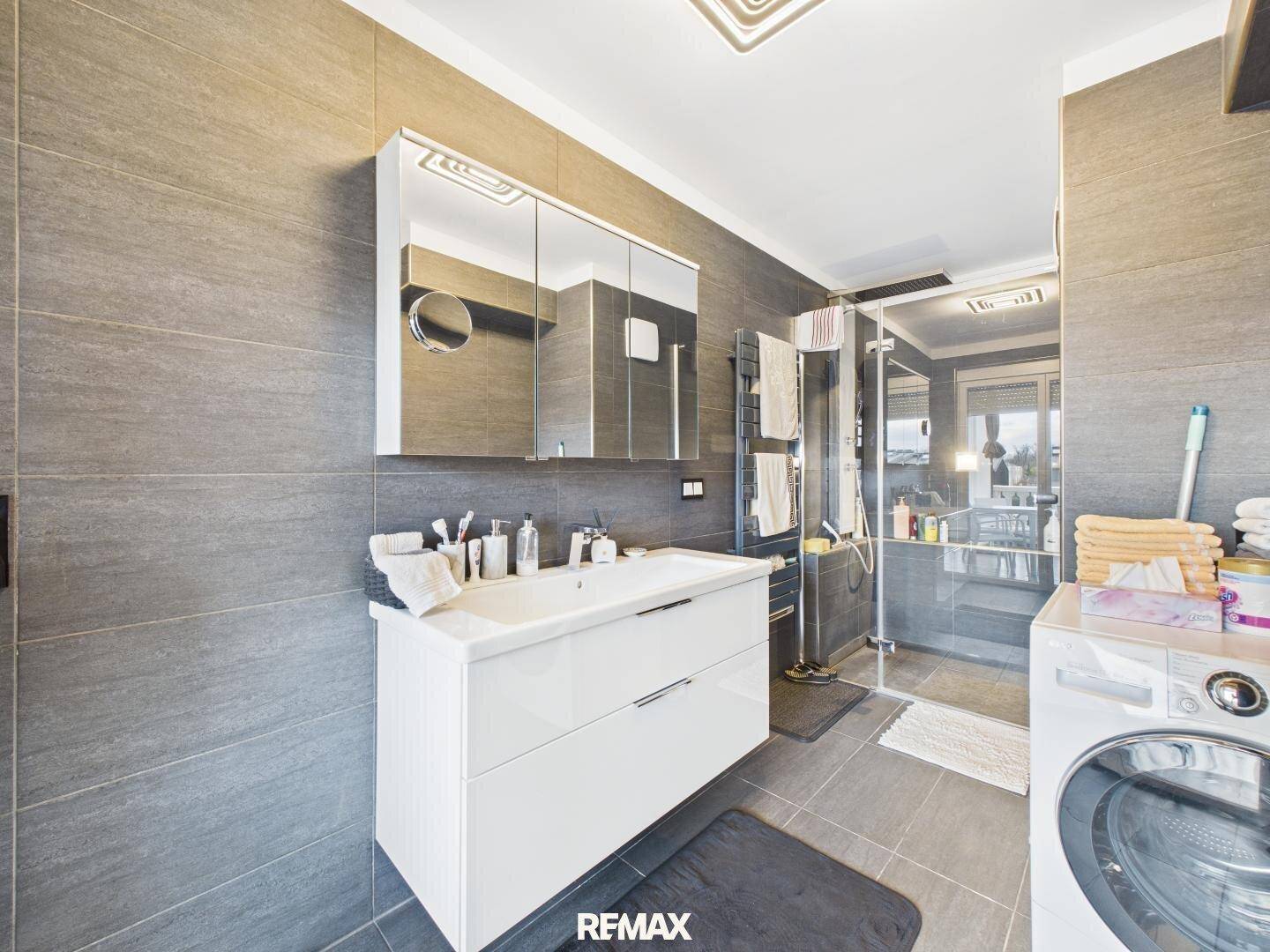 Modernes Badezimmer mit grauen Fliesen, Waschtisch und begehbarer Dusche.