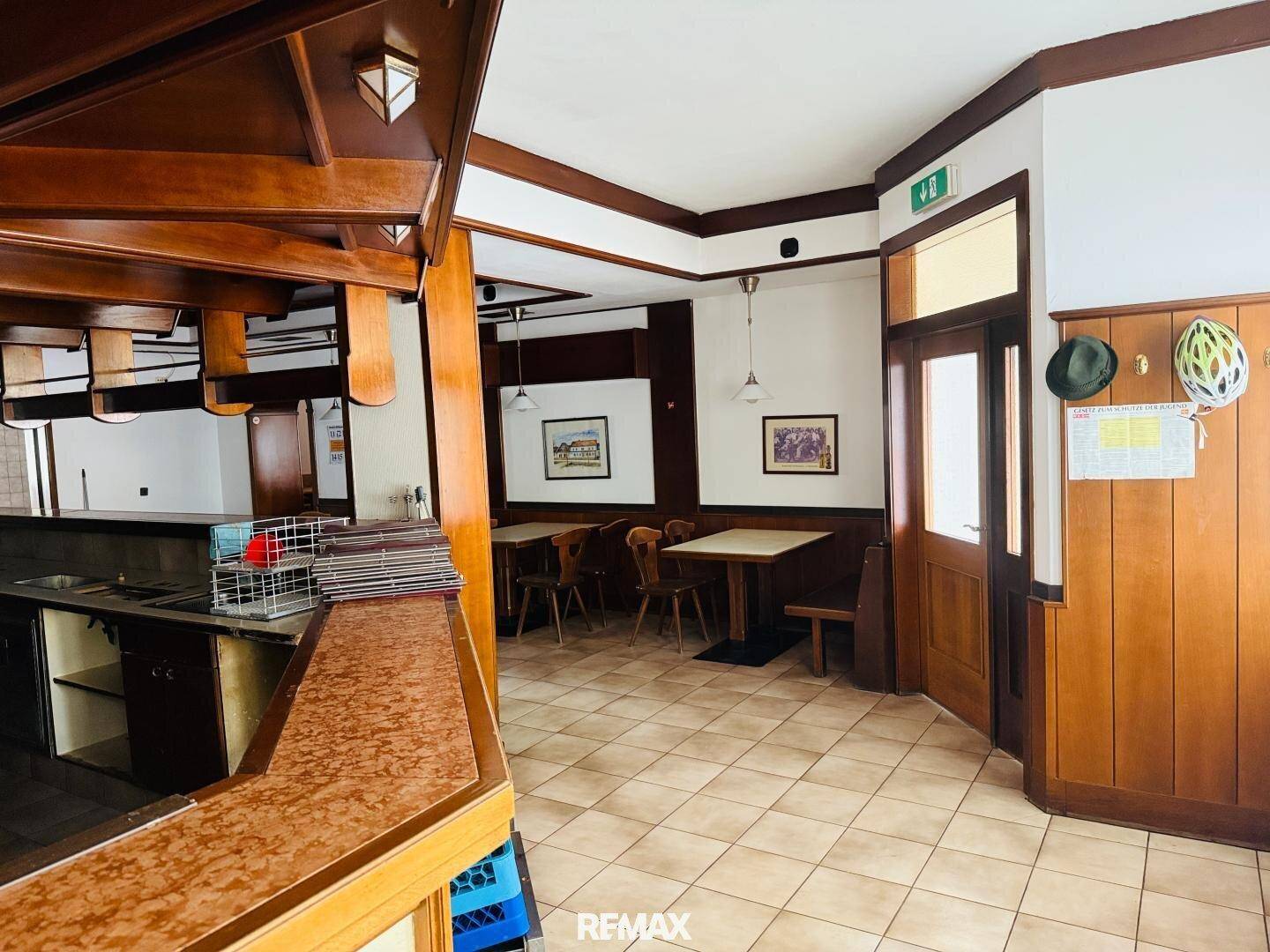 Innenansicht eines Restaurants mit Holztäfelung, gefliestem Boden und Tischen mit Stühlen.