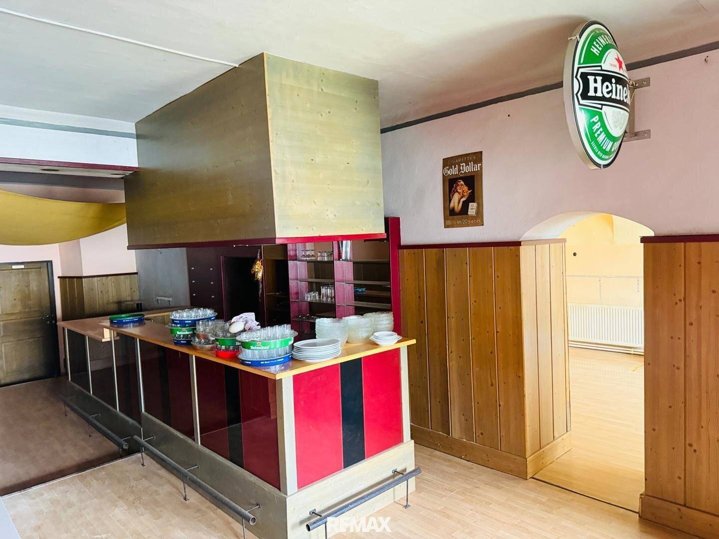 Moderner Bar-Bereich mit roter und schwarzer Theke, Holzverkleidung und einem Heineken-Schild.